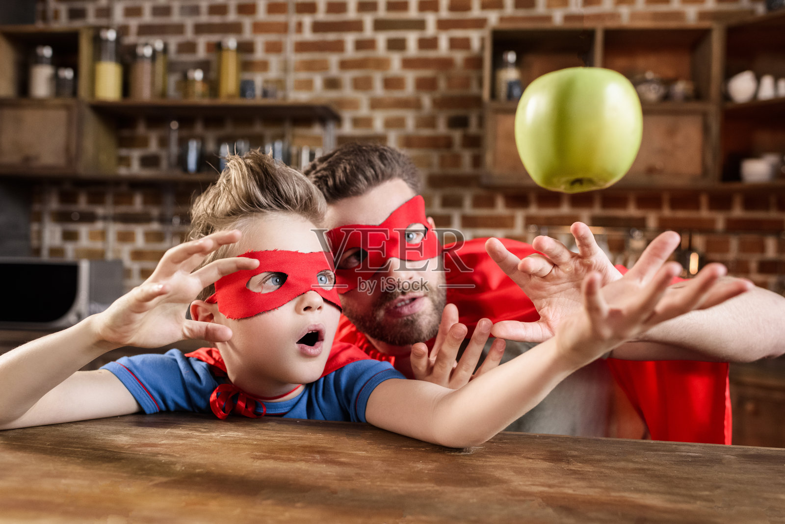 父亲和儿子穿着红色超级英雄服装玩苹果照片摄影图片