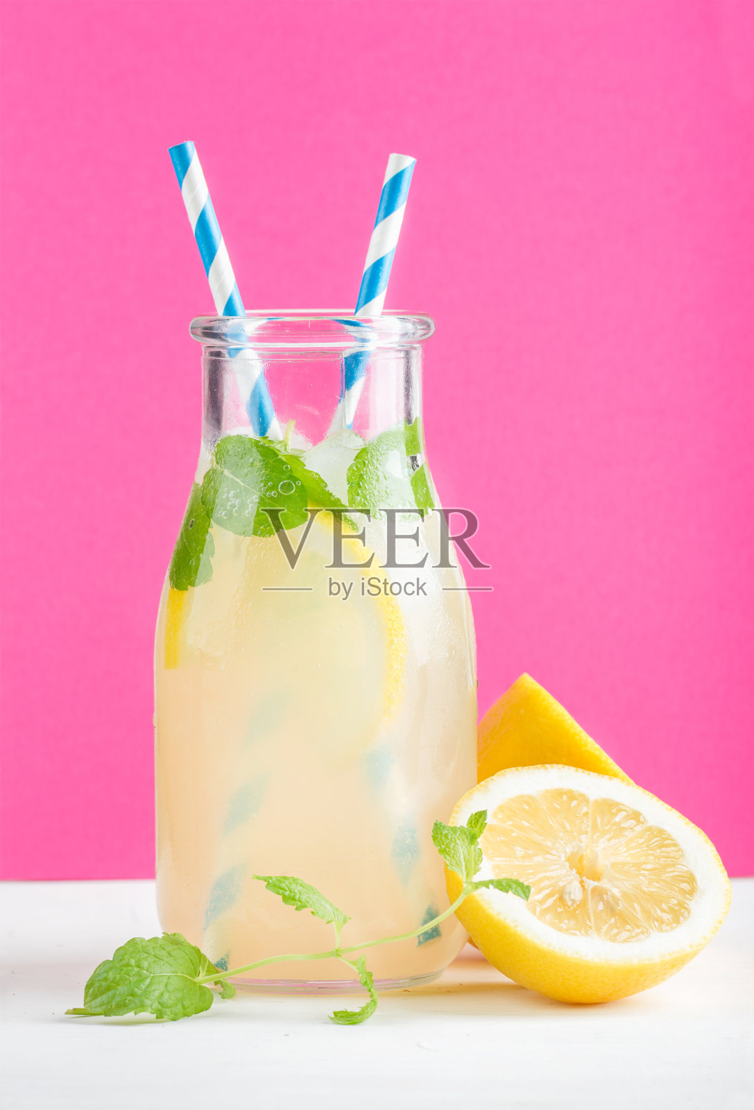 一瓶自制柠檬水，配薄荷、冰、柠檬、纸吸管和亮紫色背景照片摄影图片