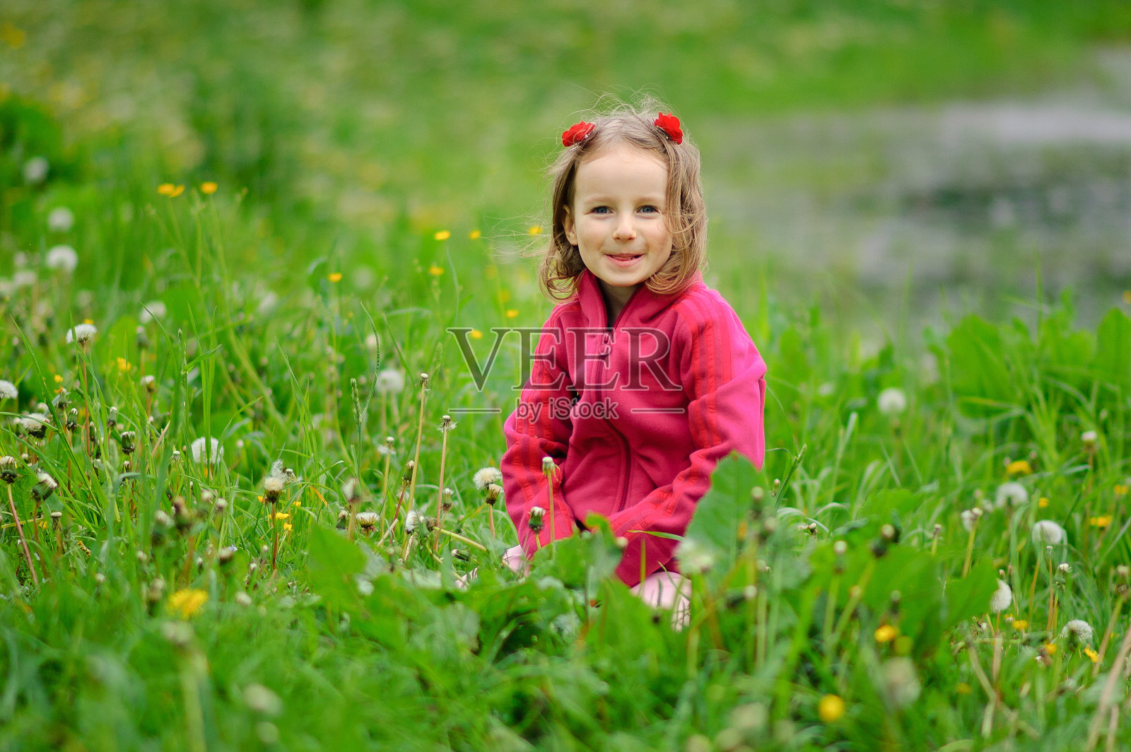 一个女孩坐在河边的湖边的草地上。孩子严肃地看着镜头。集中注意力，卷发，羊毛外套。儿童保护的一天照片摄影图片