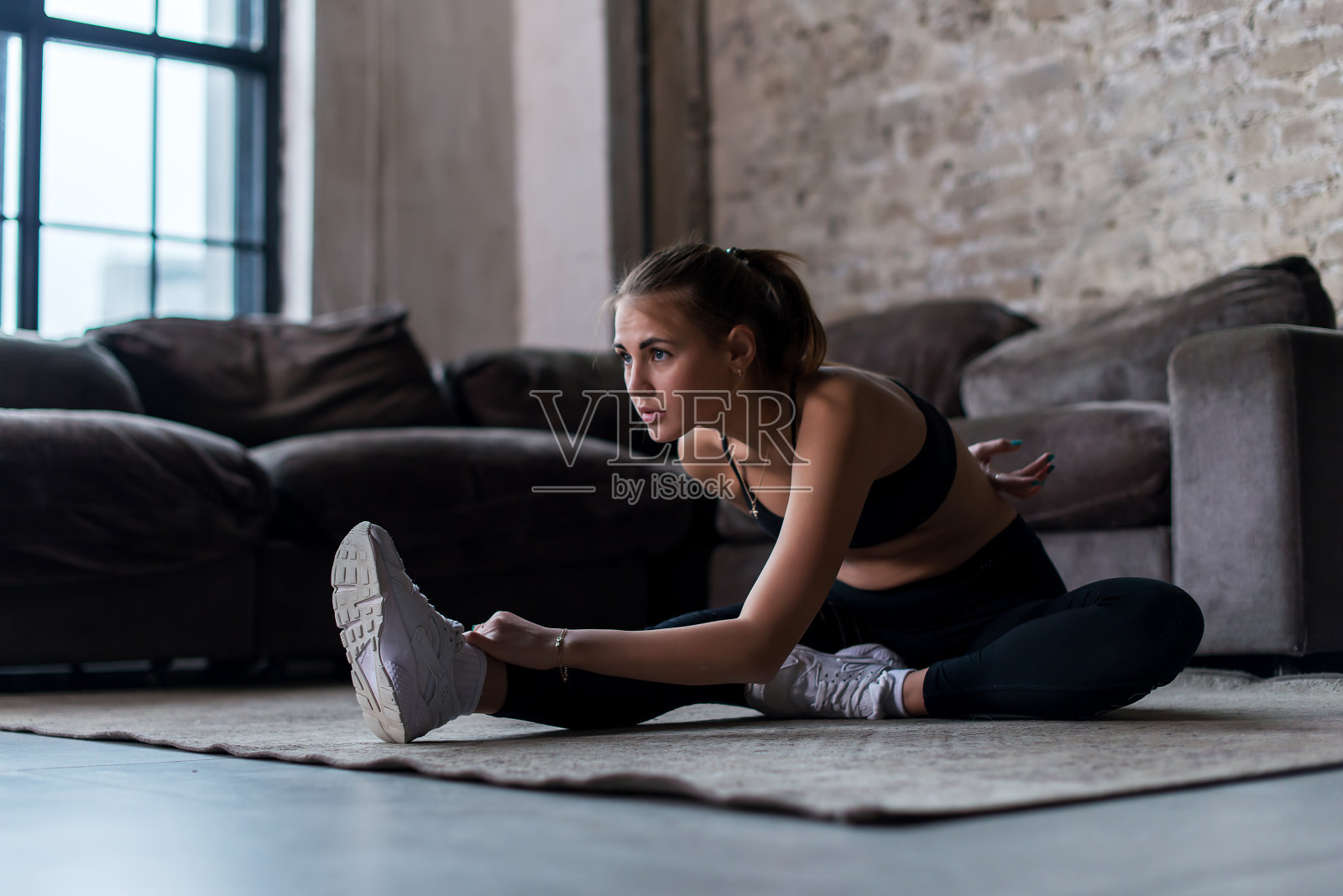 苗条的女运动员穿着运动服，在锻炼前锻炼肌肉，坐在家里的地板上做伸展运动照片摄影图片