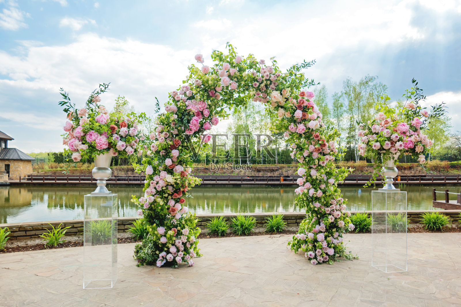 婚礼上美丽的花拱门。装着粉红玫瑰和牡丹的花瓶。婚礼安排在户外公园附近的池塘。照片摄影图片