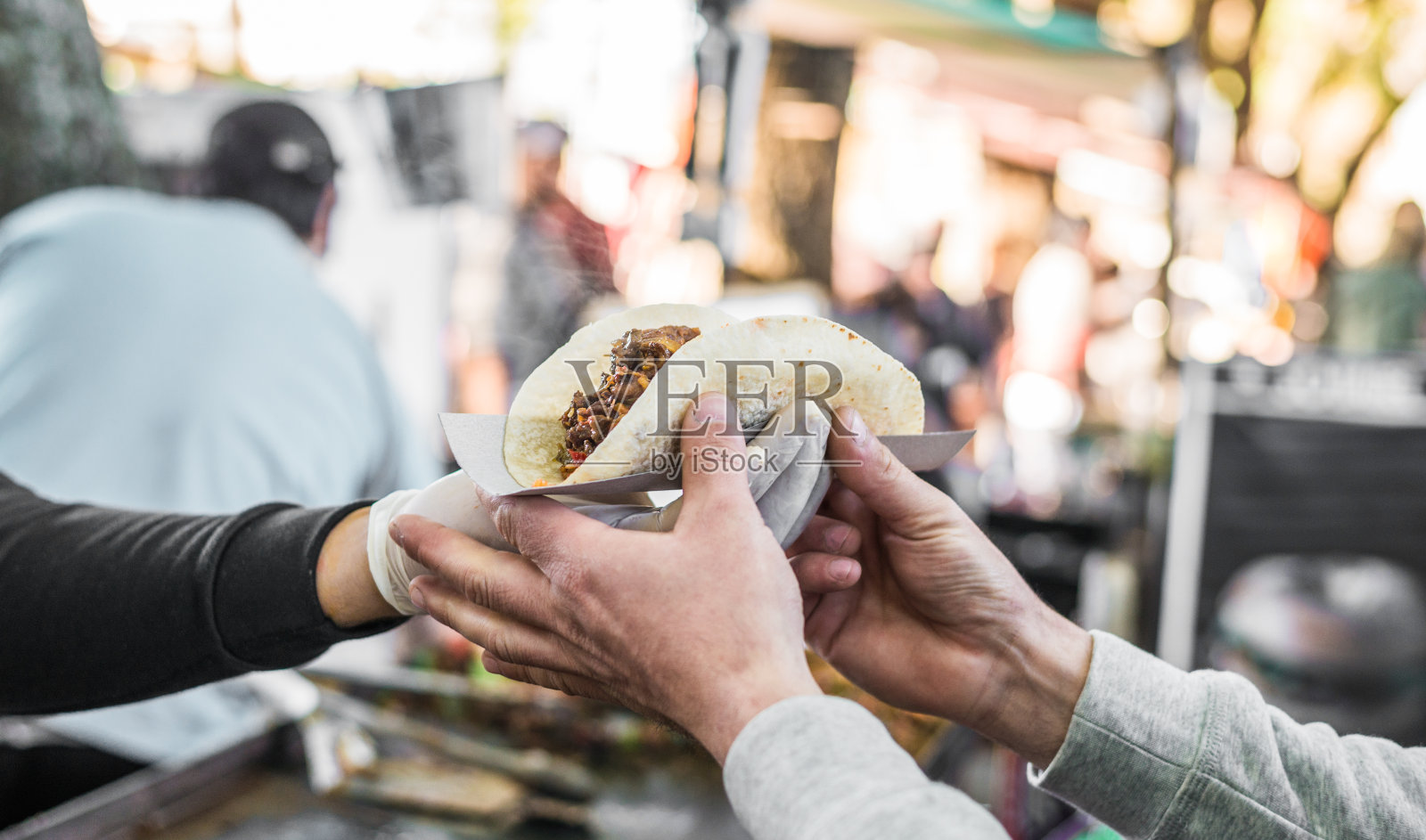 在街头小吃市场，厨师将一个墨西哥卷递给一个吃货照片摄影图片