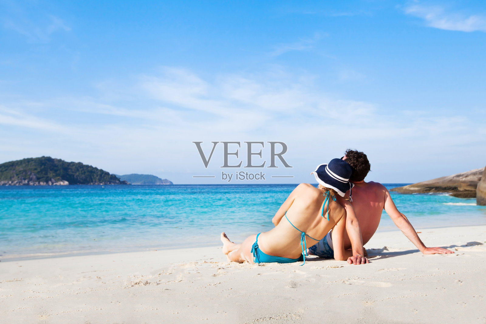 暑假，一对情侣坐在天堂般的海滩上照片摄影图片
