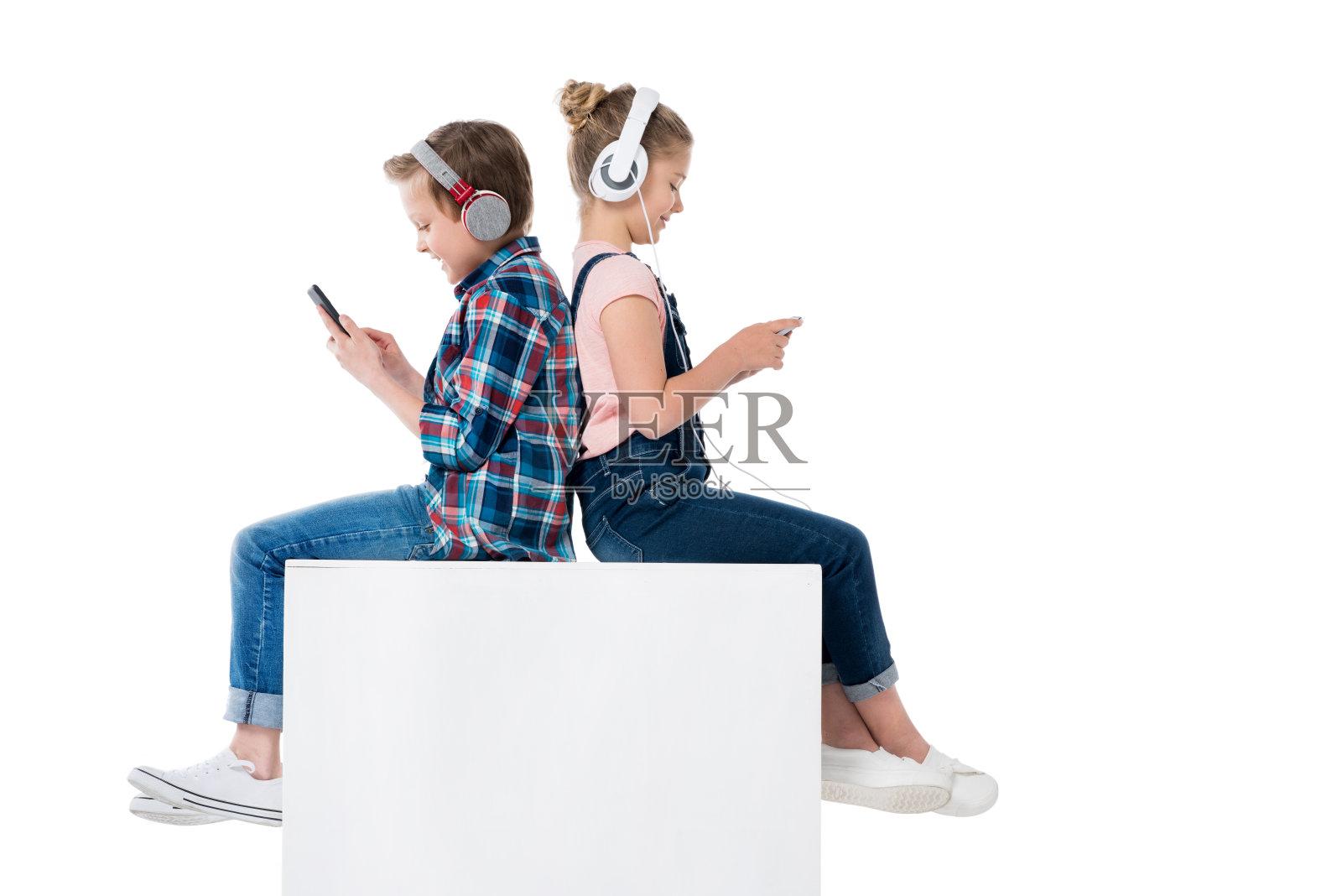 孩子们戴着耳机玩智能手机，一起坐在隔间里，被白色隔离照片摄影图片
