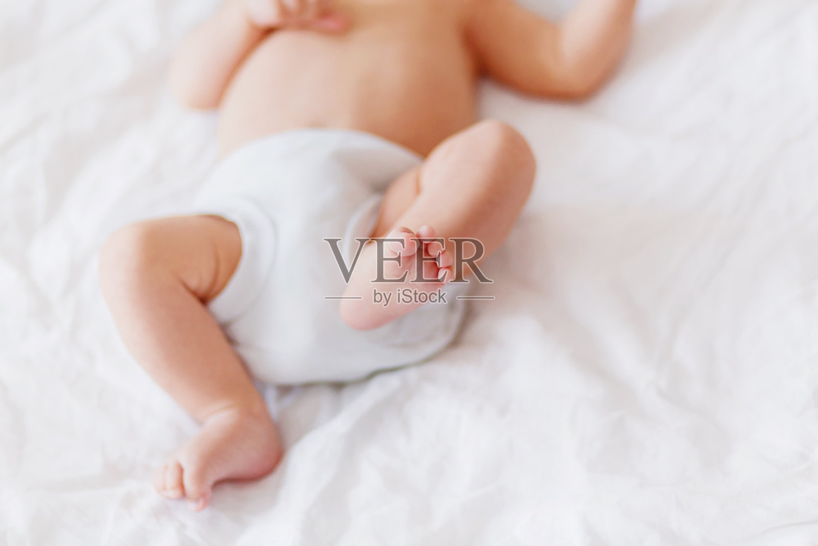 宝宝的脚。穿着白色紧身衣和尿布的小孩。在家舒适的晨间睡觉时间。照片摄影图片