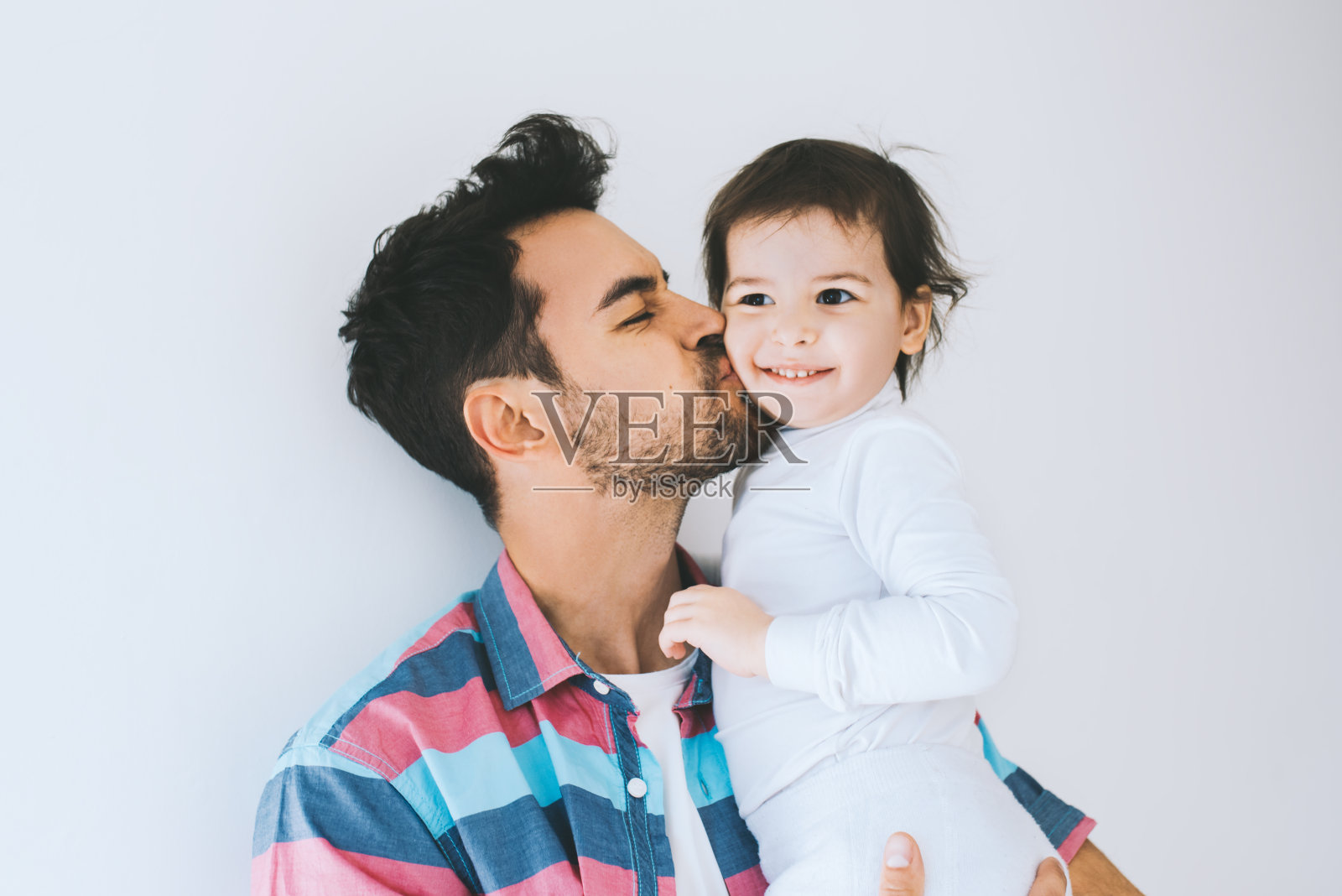 时髦的父亲亲吻他的小女儿的吸引人的近距离肖像。年轻的爸爸正在享受和孩子在一起的时光。英俊的父亲带着小女孩。快乐的父女。家庭生活方式。照片摄影图片