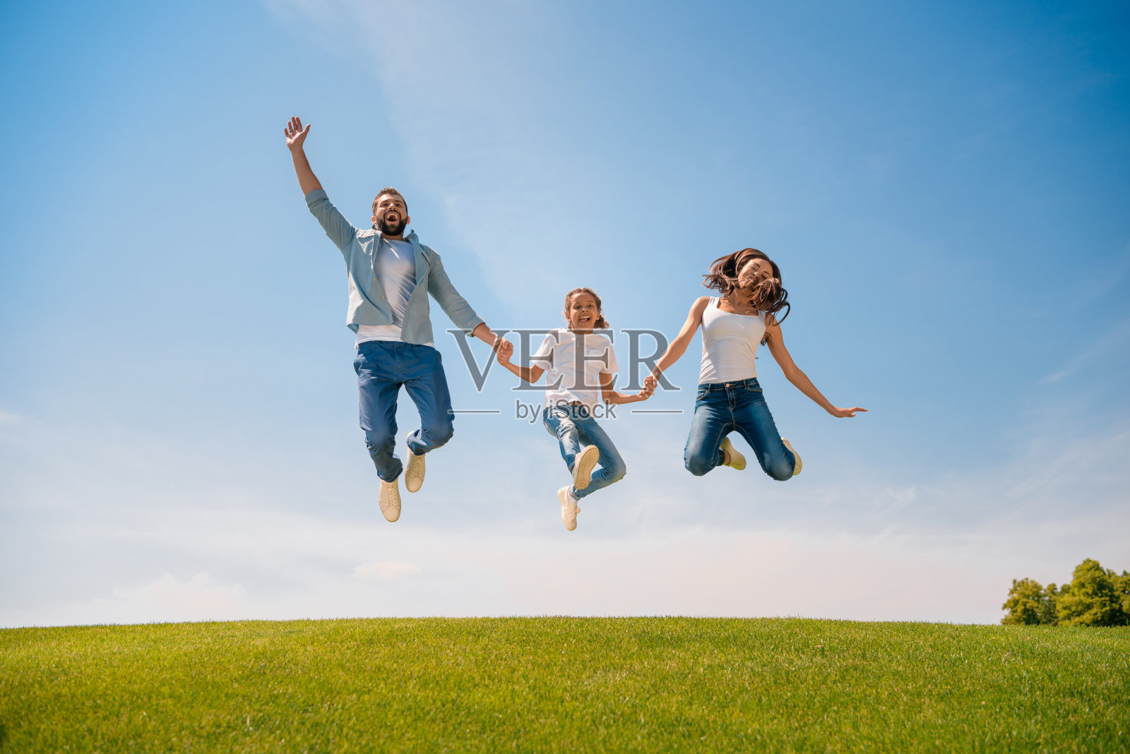 幸福的年轻家庭和一个孩子手牵着手，在草地上跳跃照片摄影图片