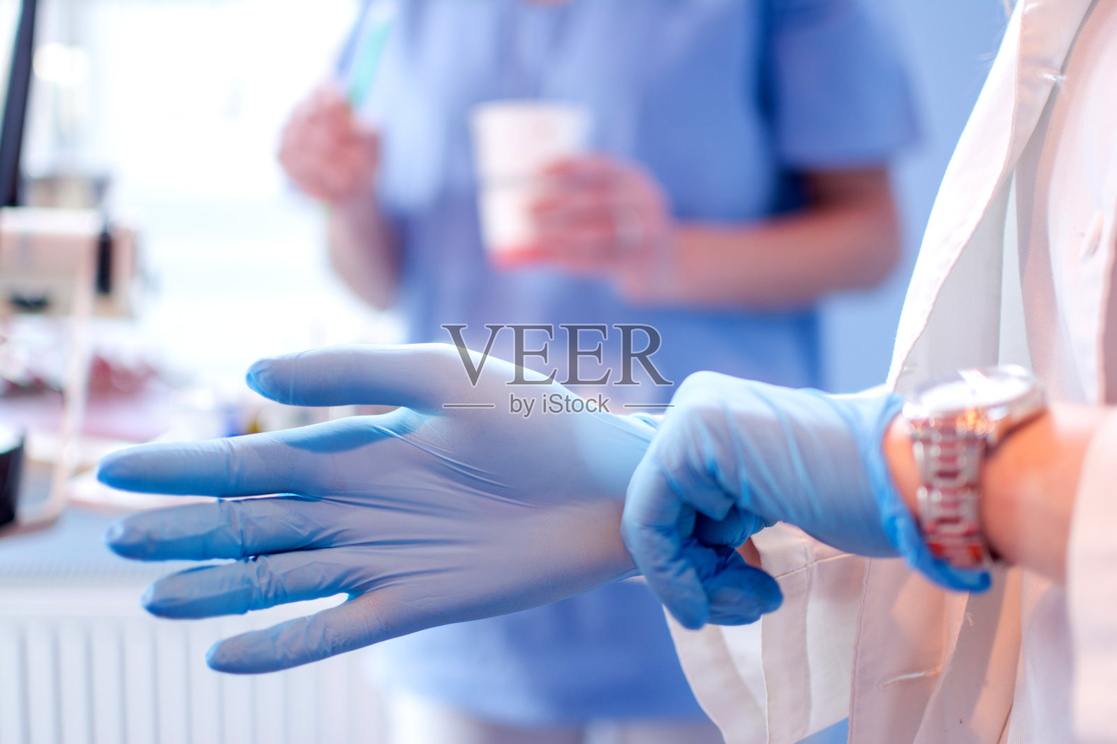女性医生的双手在医疗诊所里戴上蓝色消毒手术手套的特写。照片摄影图片