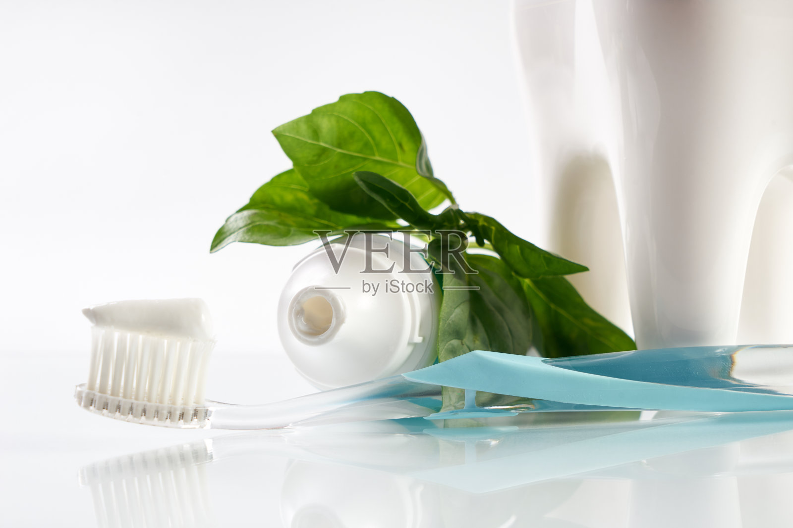 一个草药牙膏在牙刷上的特写与白色健康的陶瓷牙齿模型，管和绿色草药孤立在白色背景与复制空间。牙科保健的概念。照片摄影图片