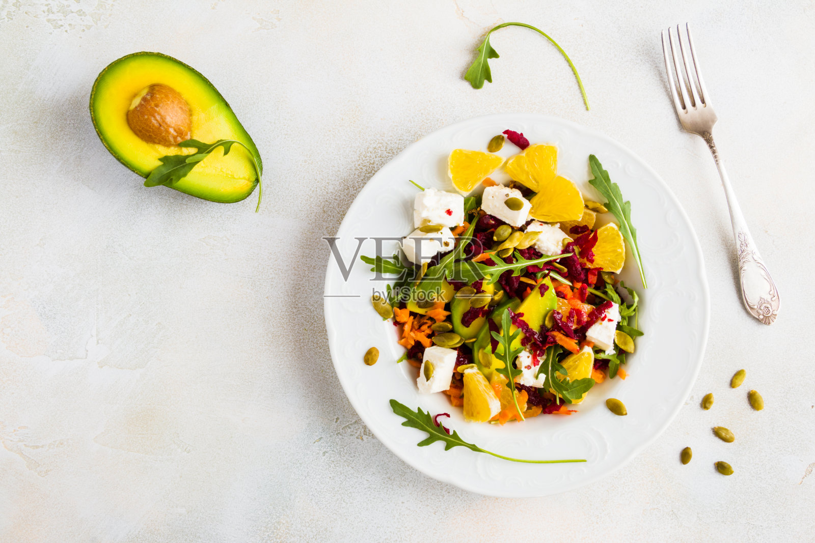 健康的素食沙拉，配有生甜菜根，胡萝卜，芝麻菜，鳄梨，橙子，奶酪和南瓜子。照片摄影图片