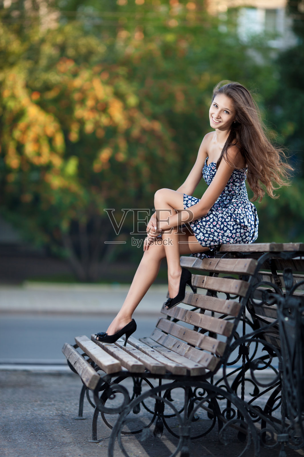 漂亮的黑发女子坐在长凳上。城市背景照片摄影图片