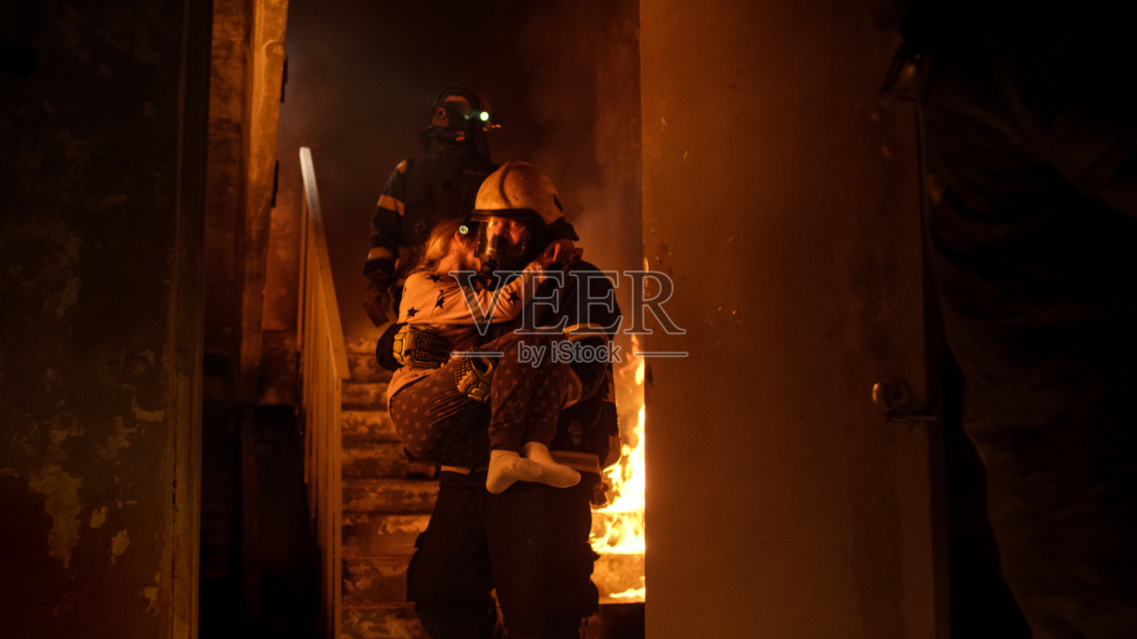 勇敢的消防员抱着一个被救下的女孩走下燃烧的大楼的楼梯。照片摄影图片