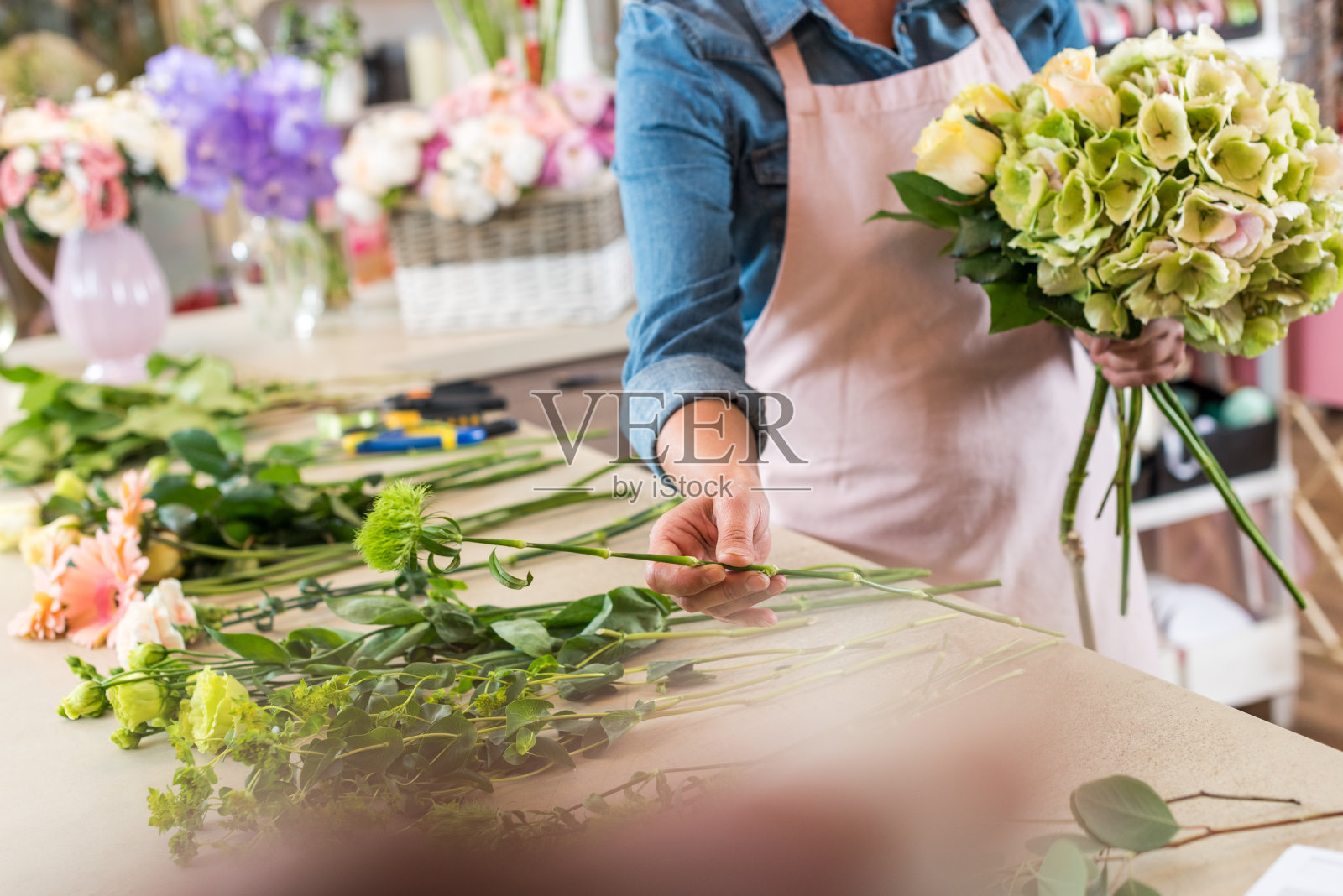 裁剪照片的年轻花商在围裙工作与鲜花和安排花束照片摄影图片