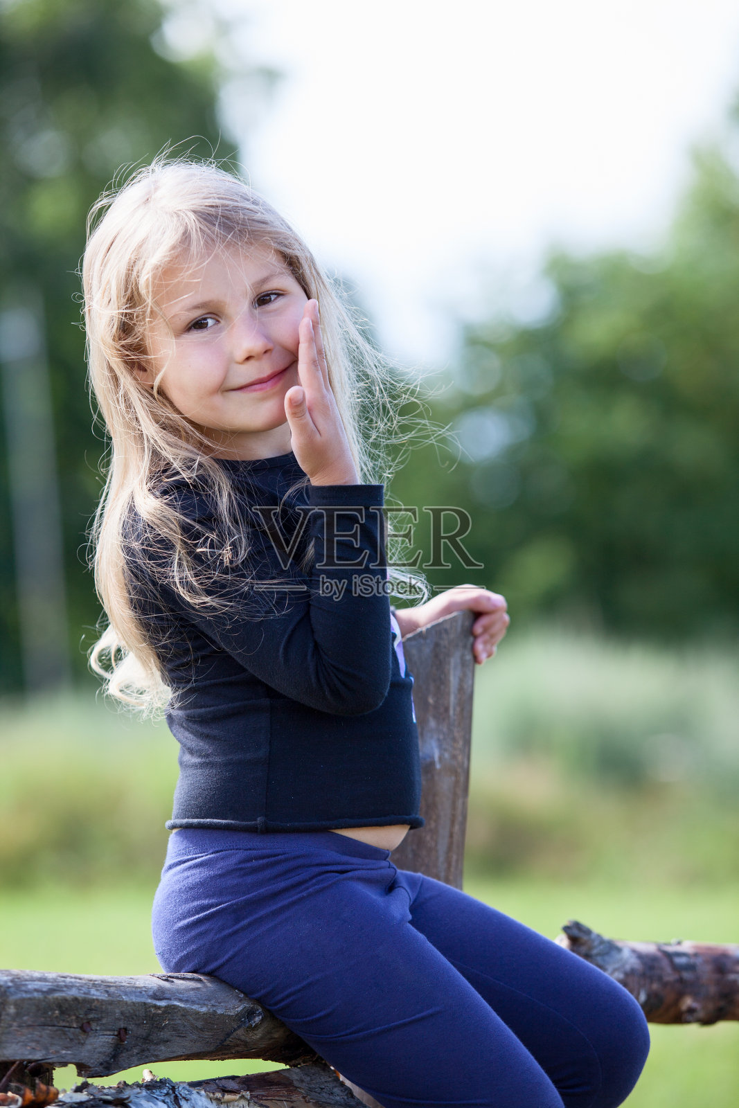 摆姿势的小白人女孩坐在村庄的篱笆上照片摄影图片