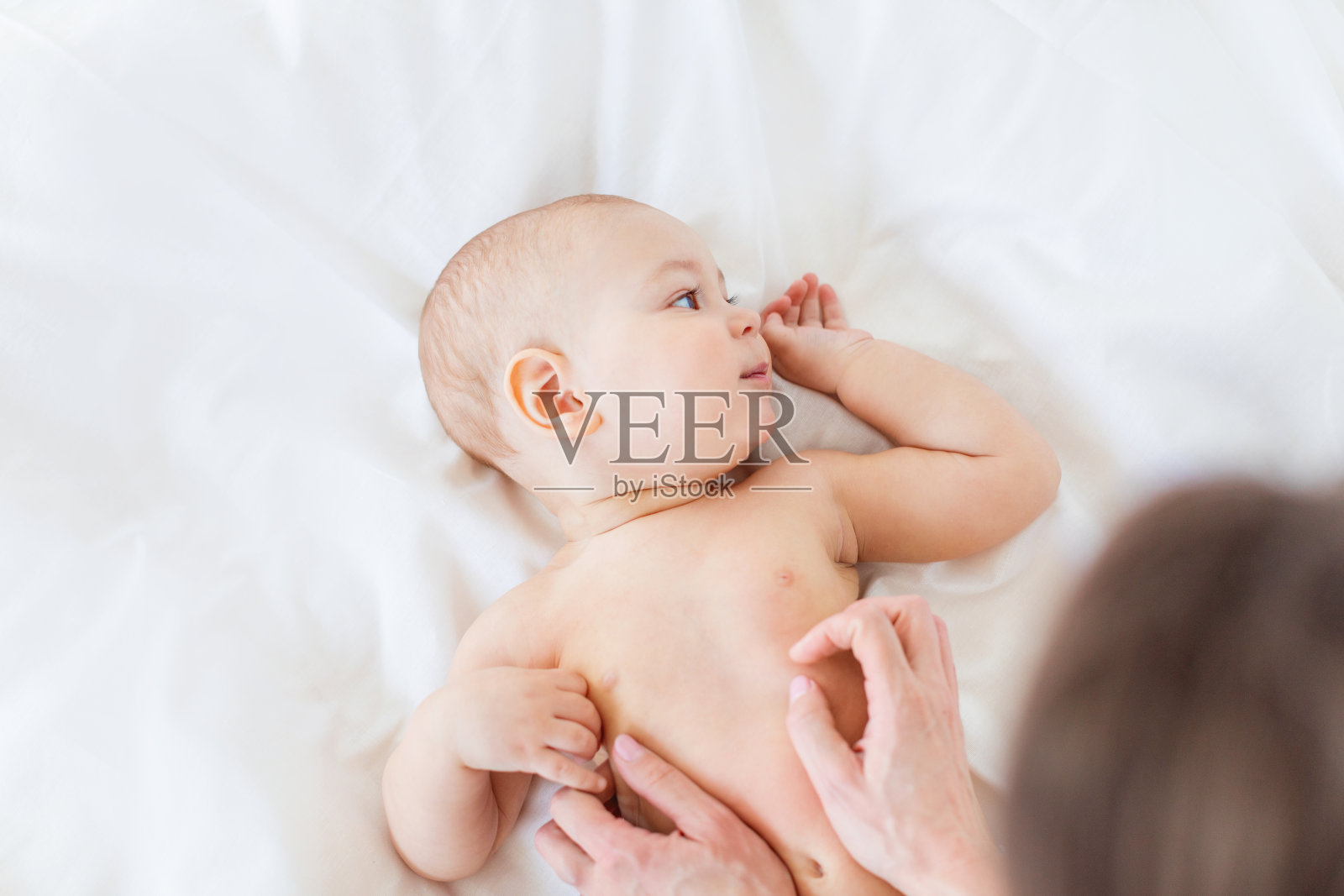 妈妈给躺在床上的可爱新生儿按摩的镜头，1岁的婴儿概念照片摄影图片
