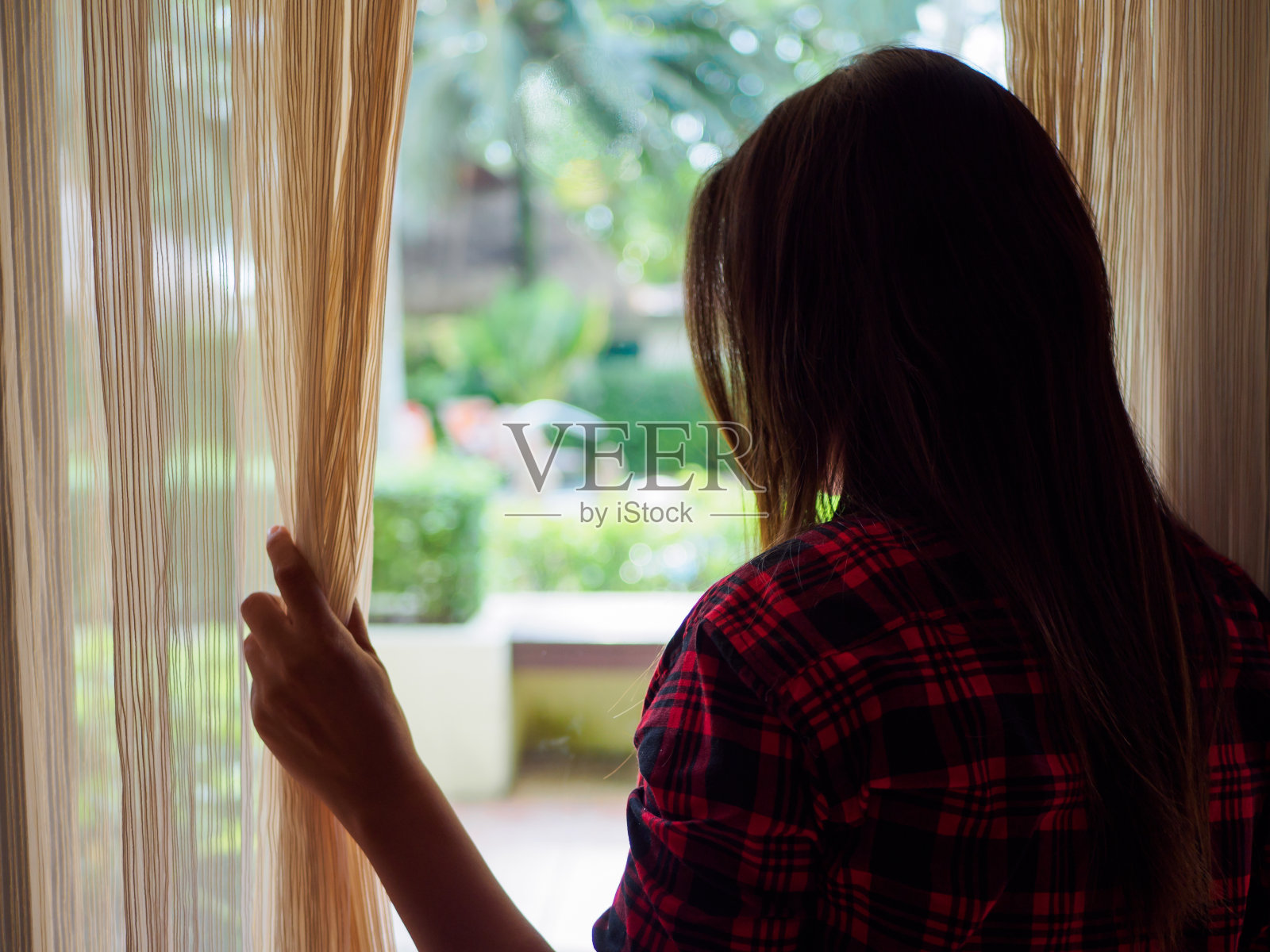 一个年轻女人的后视图，拉着窗帘打开看出一个大的光窗户在家里照片摄影图片