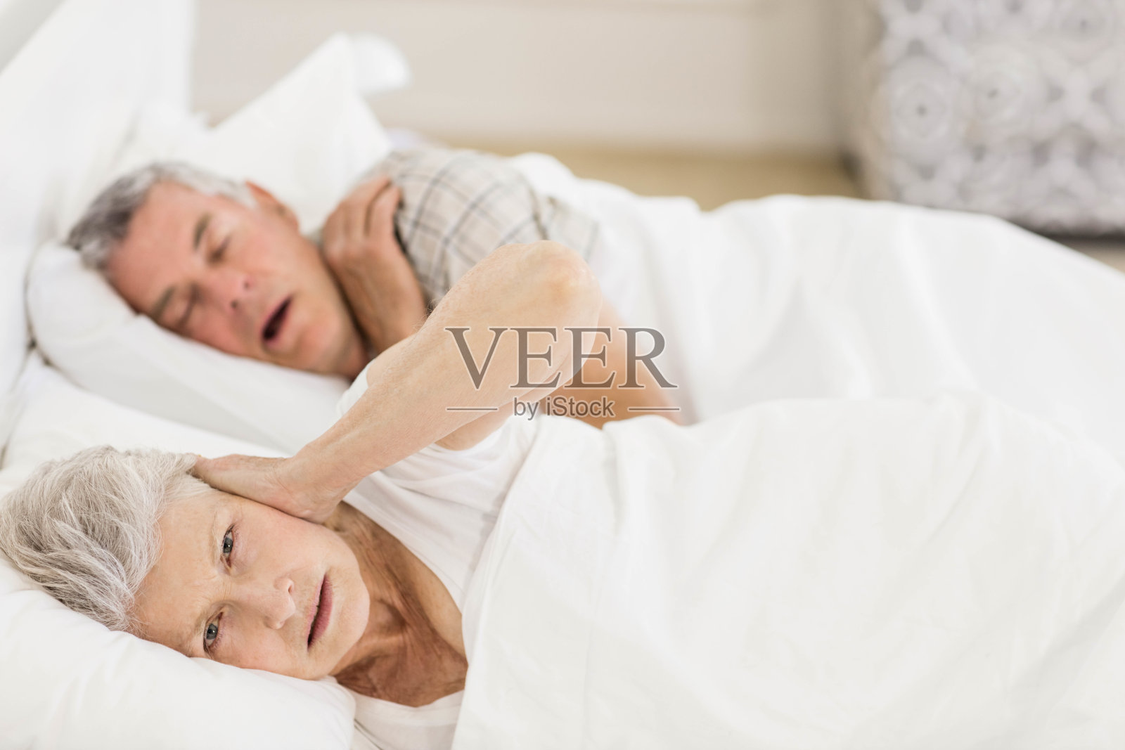 醒着的老女人在床上捂着耳朵照片摄影图片