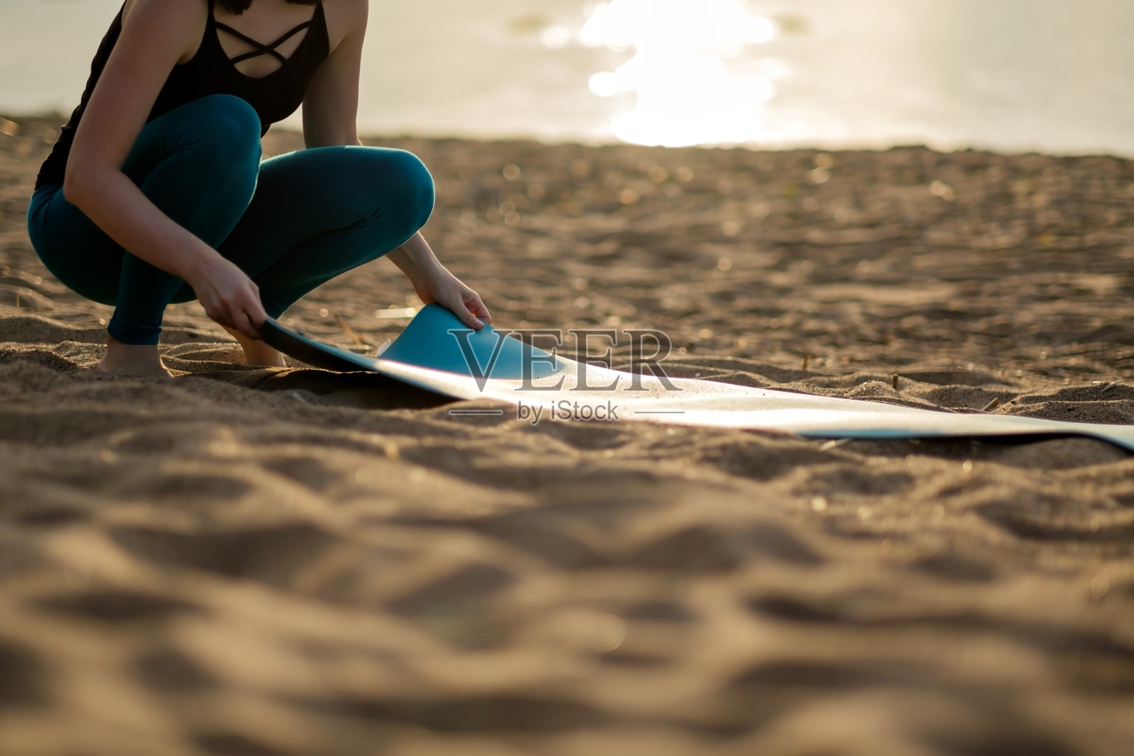 迷人的年轻女子折叠绿色瑜伽或健身垫子后，在海滩上锻炼。照片摄影图片