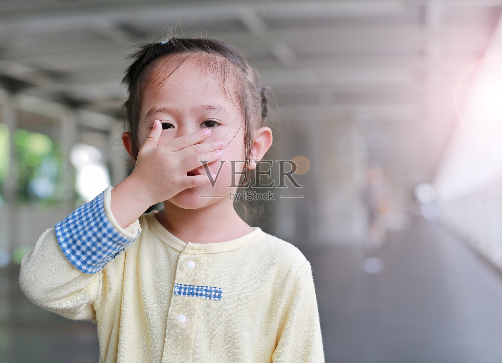 一个亚洲小女孩用手捂住自己的嘴和鼻子。照片摄影图片
