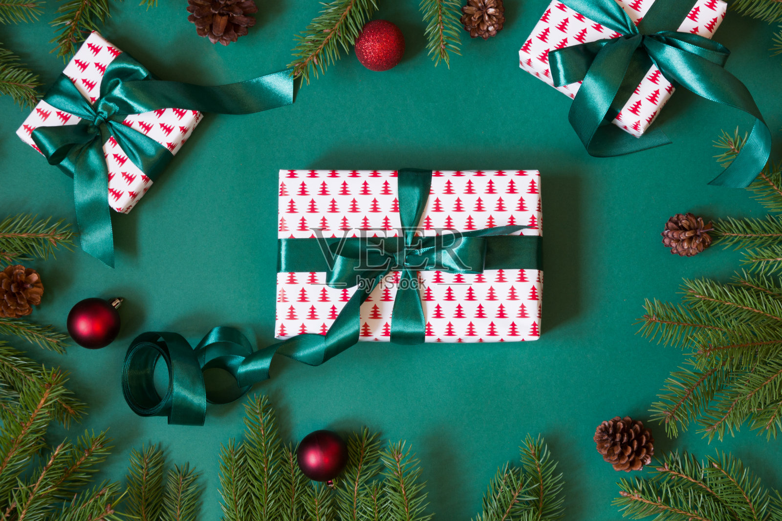 圣诞礼盒和礼物包装在设计纸和绿色丝带在绿色与红色装饰。平的。前视图。照片摄影图片