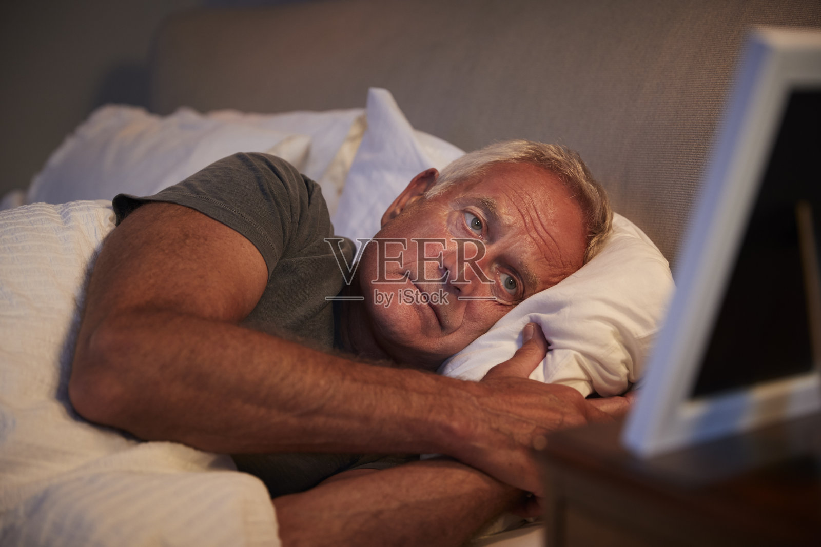 悲伤的老人躺在床上看相框照片摄影图片