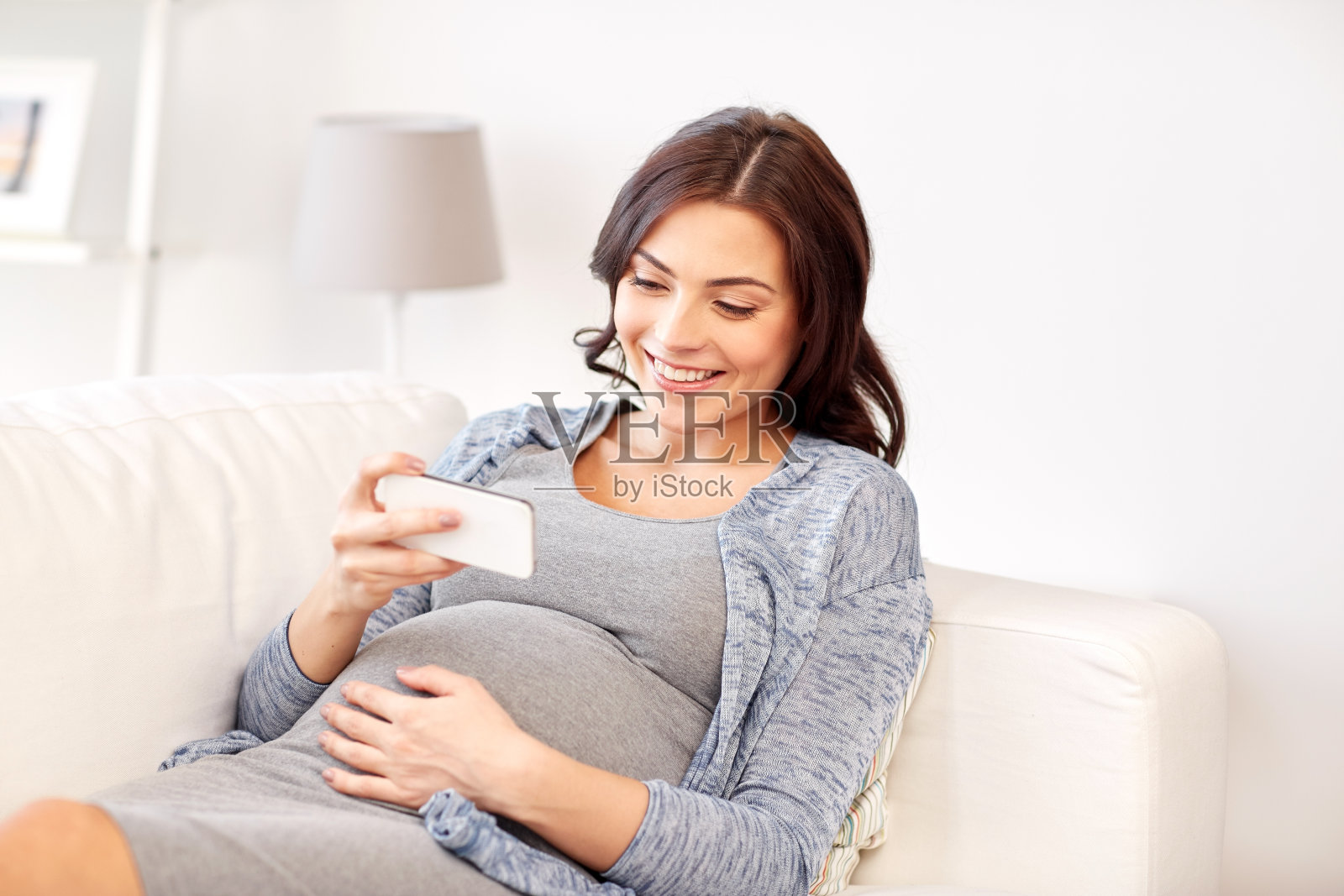 快乐的孕妇在家里用智能手机照片摄影图片