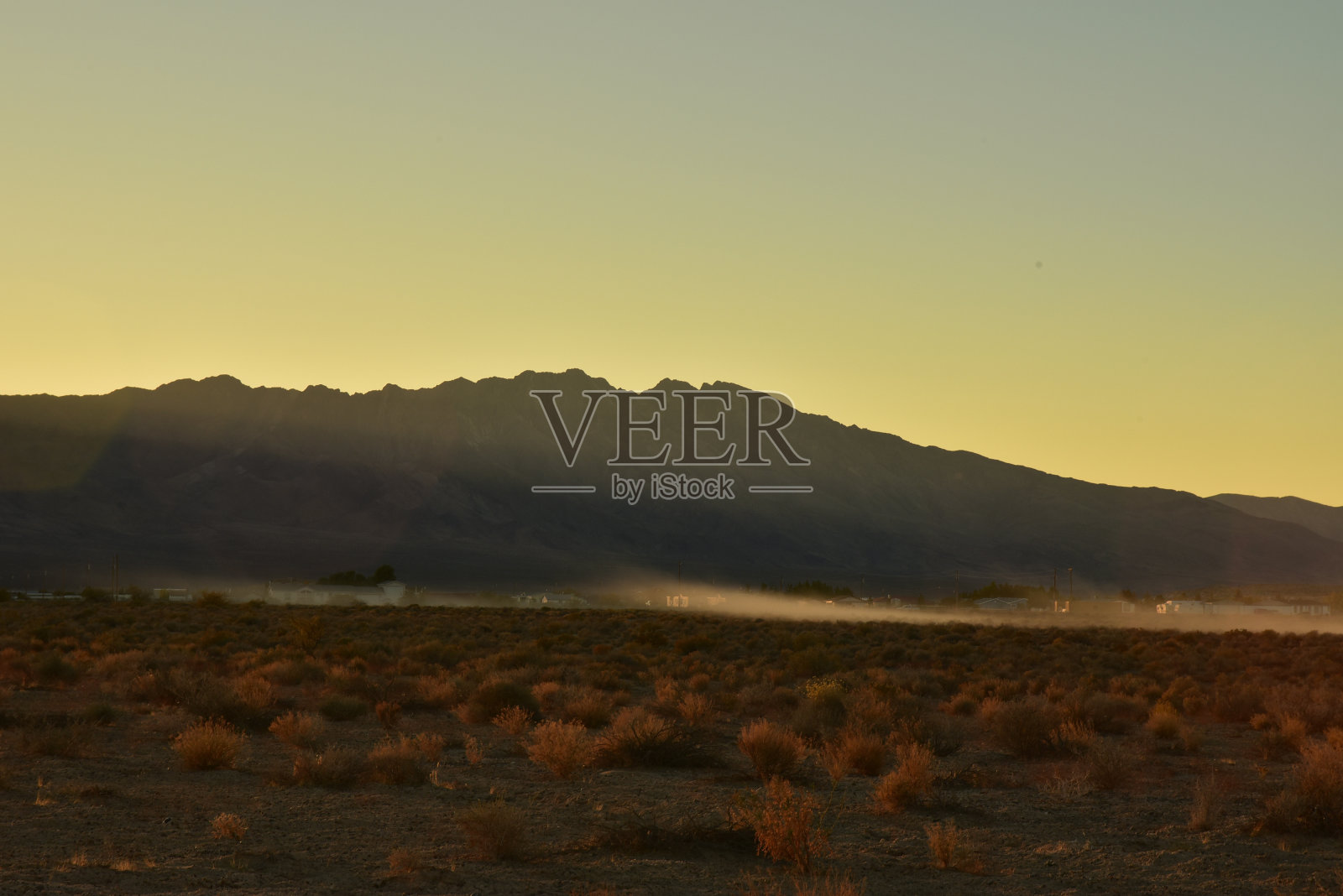在山脚下的沙漠中，车辆驶过尘土飞扬的小路照片摄影图片