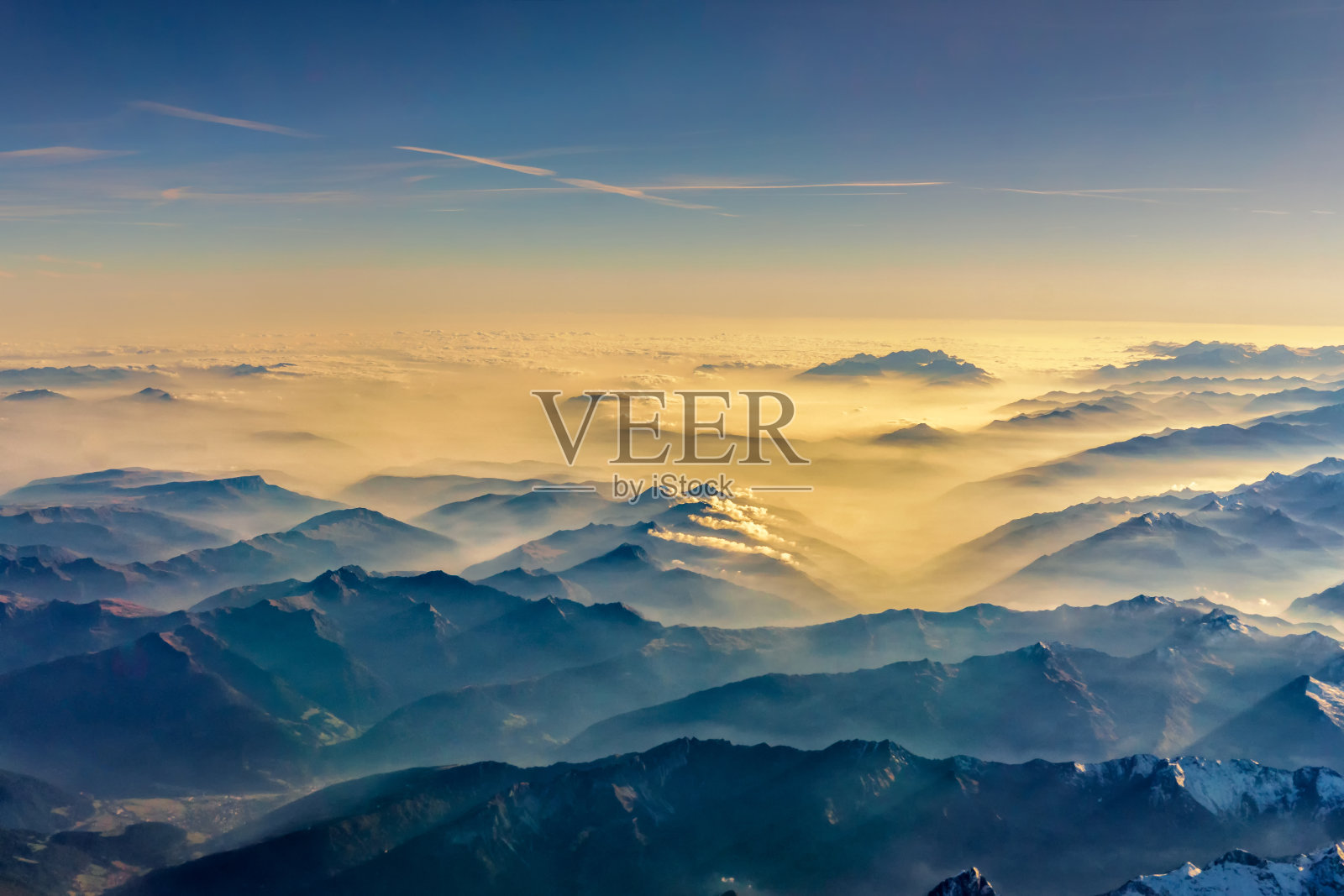 从飞机上俯瞰，透过云层从山顶俯瞰美丽的山景。照片摄影图片