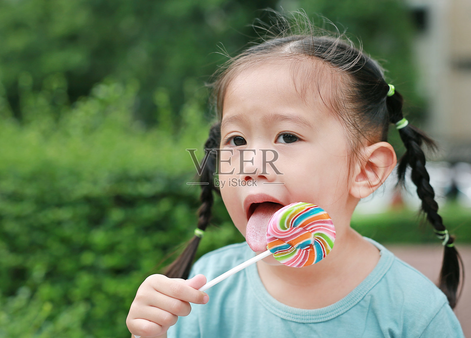 快乐的小女孩在花园里舔棒棒糖。照片摄影图片