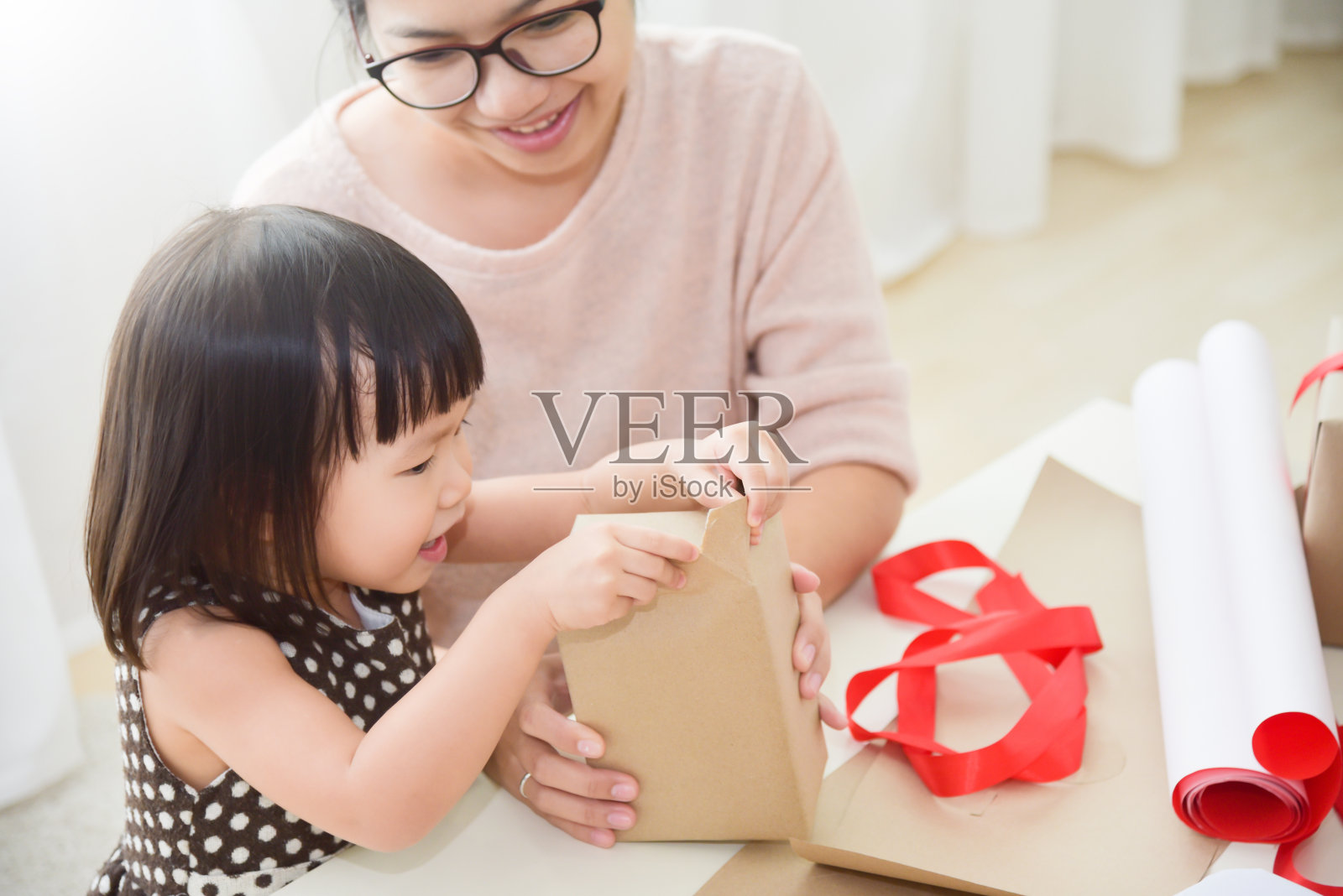 年轻的母亲和她的女儿在包装礼品盒。照片摄影图片