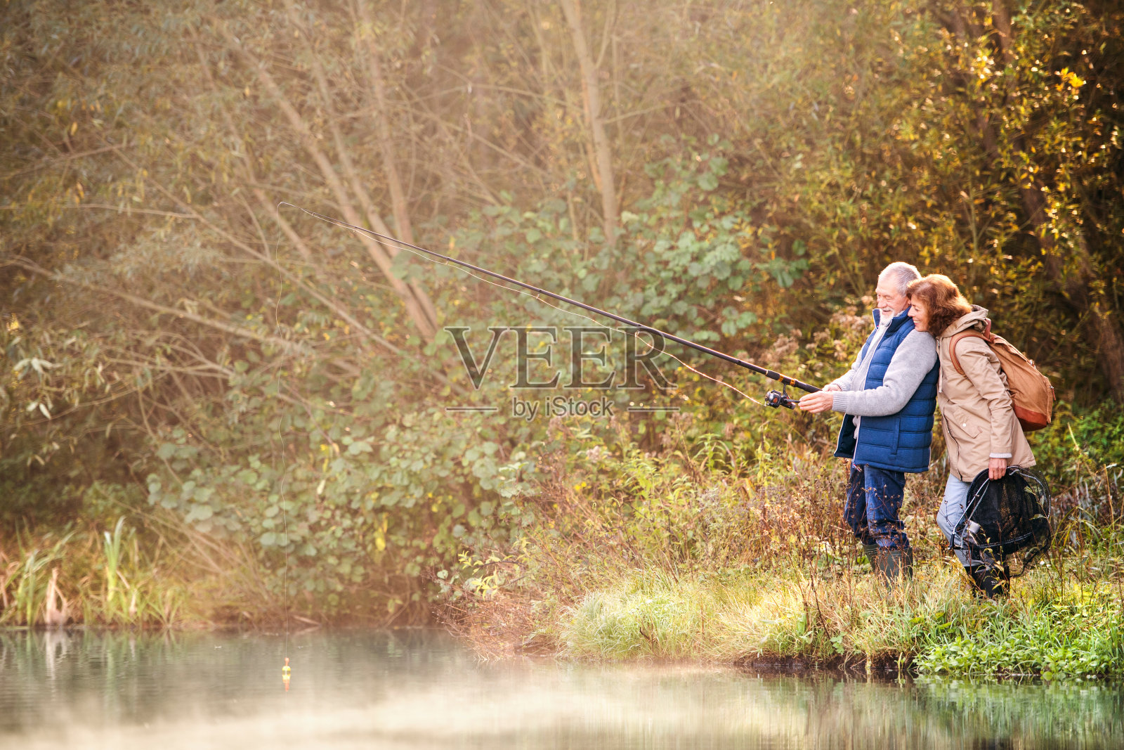 一对老年夫妇秋天在湖边钓鱼。照片摄影图片