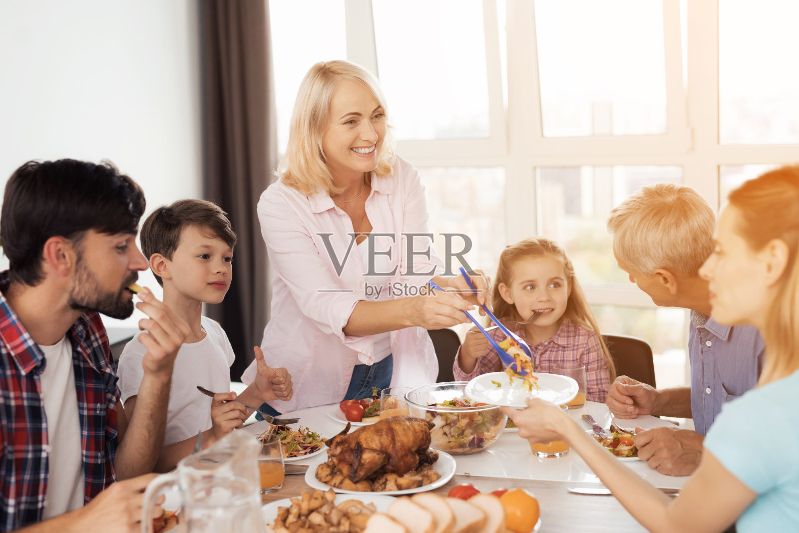 一家人在感恩节的节日餐桌上吃饭。一个女人在摆放食物，她的家人已经在吃了照片摄影图片