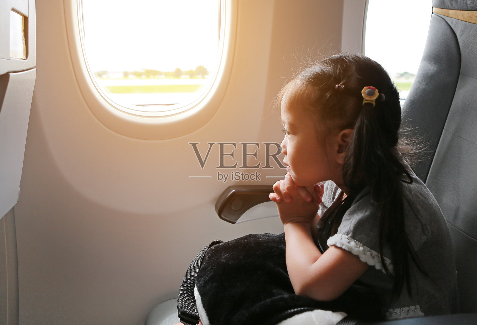 小女孩坐在飞机上，靠窗祈祷。可爱的小女孩乘飞机旅行。照片摄影图片