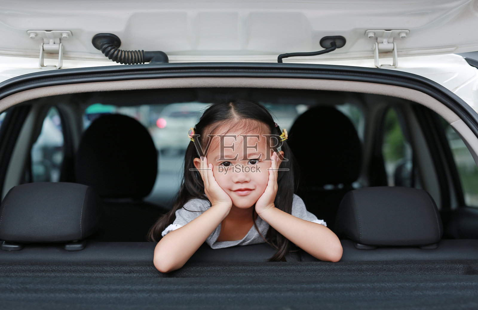 一个可爱的微笑小女孩从车的掀背门往外看。照片摄影图片