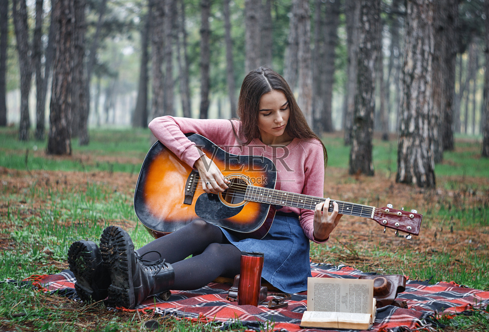 一个拿着吉他的漂亮女孩坐在树林里的毯子上照片摄影图片
