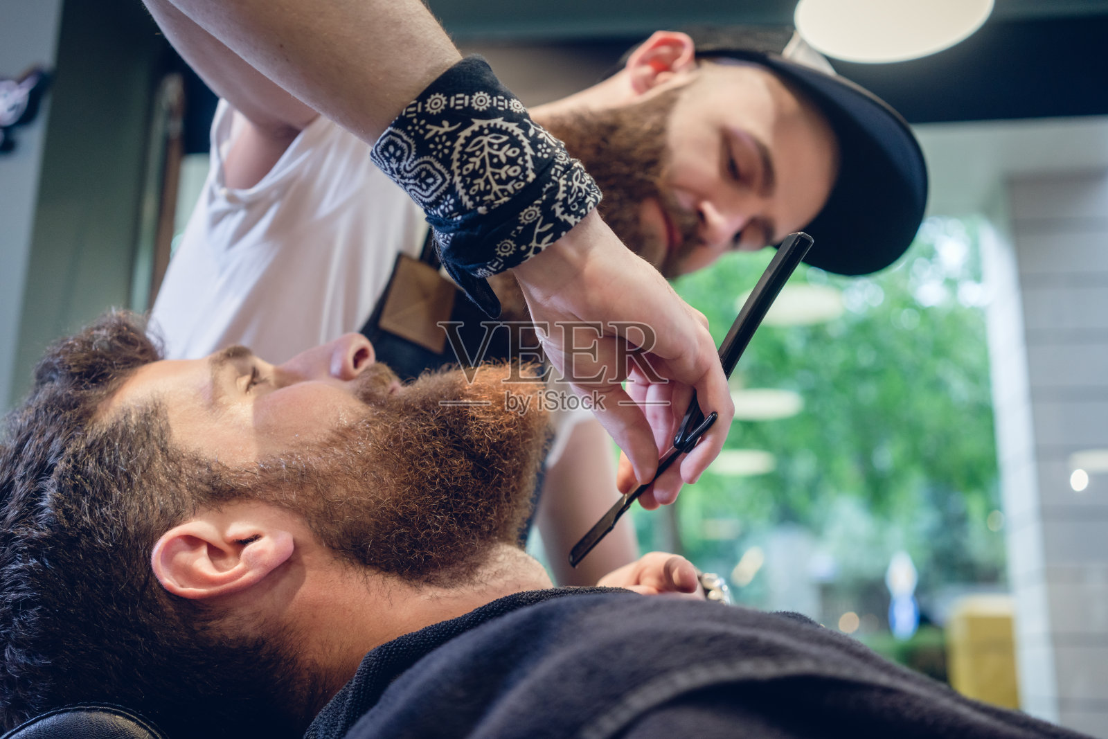 一个留着胡子的年轻人正准备在理发店里刮胡子，手里拿着一把直刮胡刀照片摄影图片