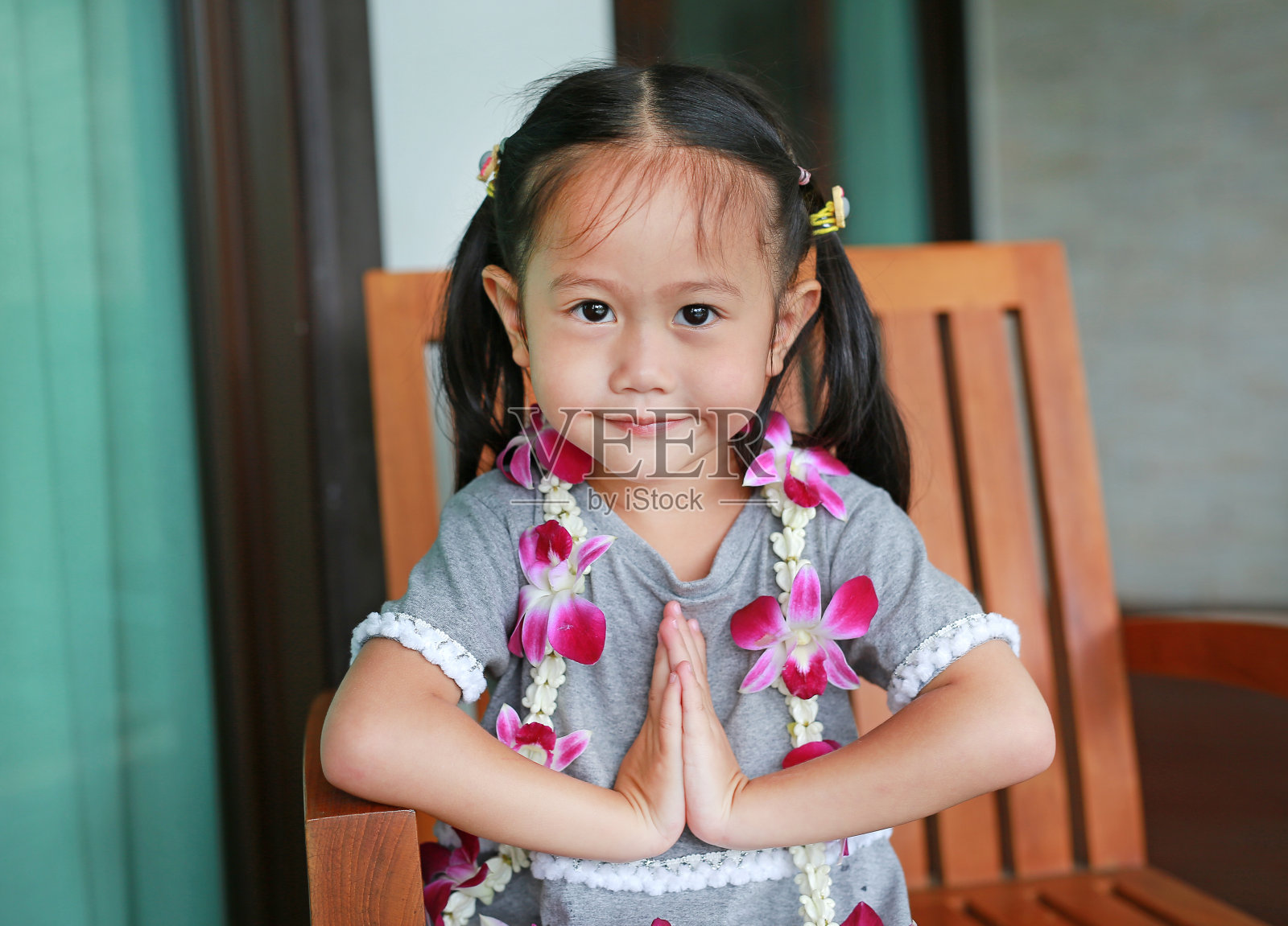 泰国小女孩“Sawatdee”坐在木椅上。照片摄影图片