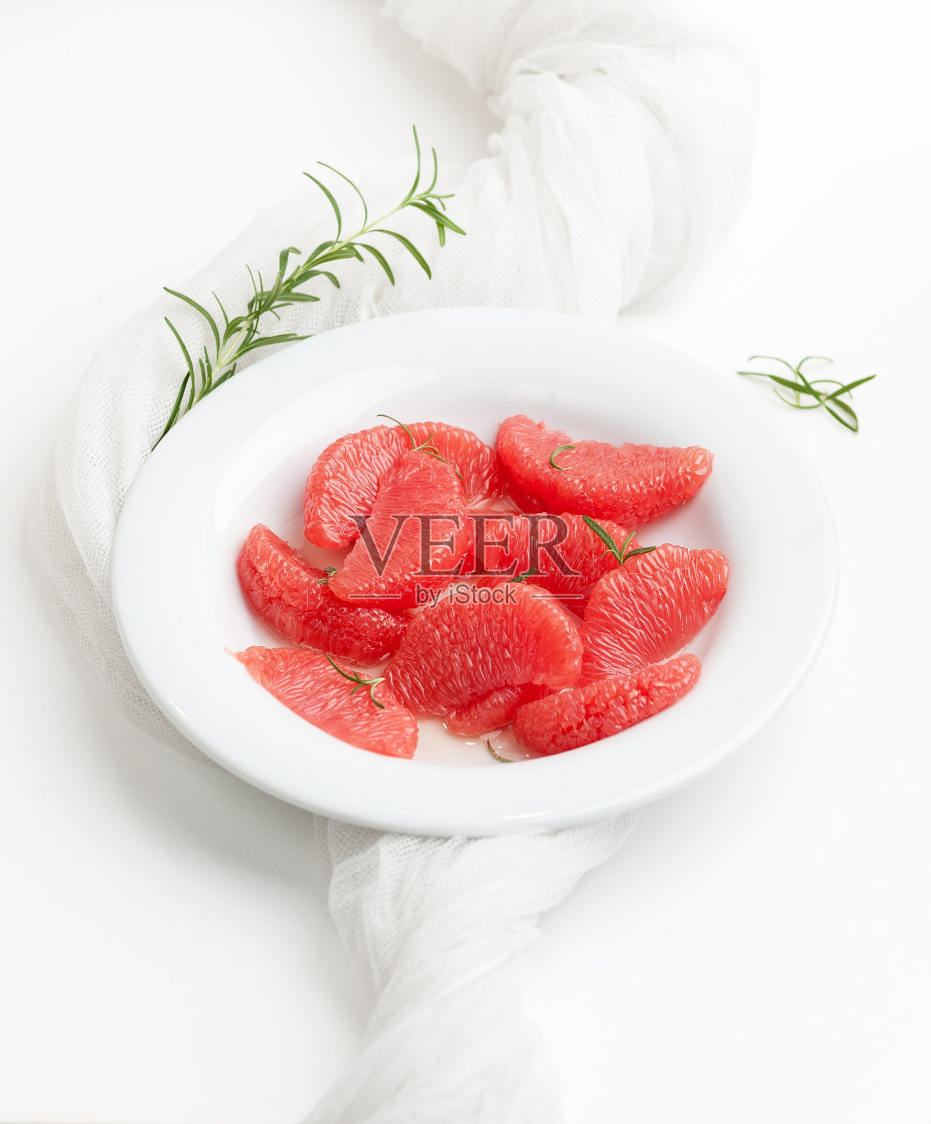 去皮葡萄柚片和迷迭香枝放在白色的盘子里，背景是白色的。照片摄影图片