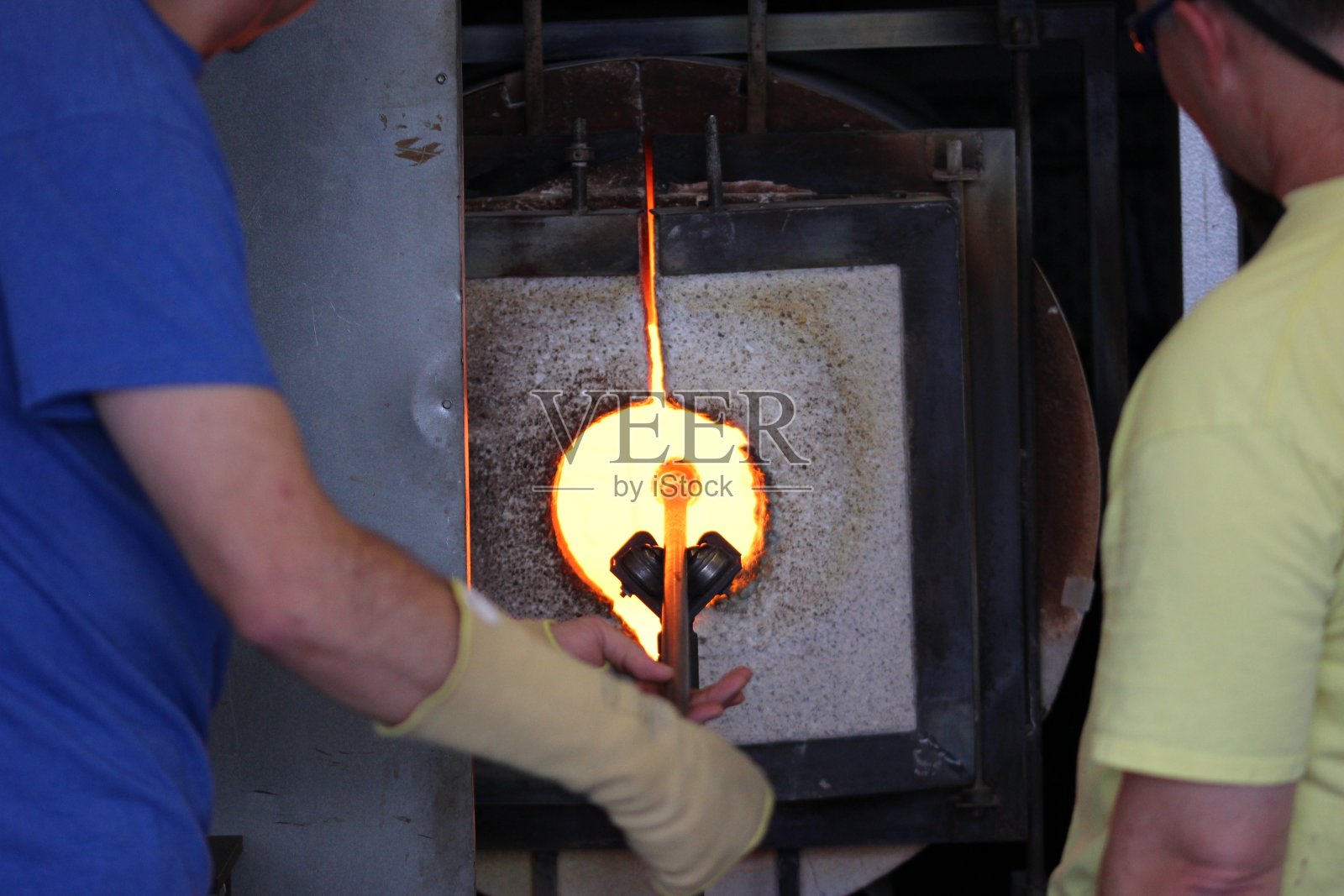 将玻璃熔在熔炉中的金属棒上用于吹制玻璃照片摄影图片