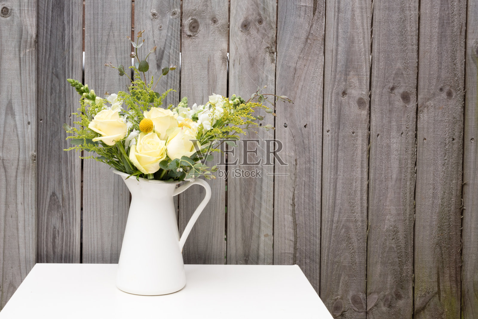 白色的桌子上放着春天的花朵，映衬着灰色的篱笆照片摄影图片