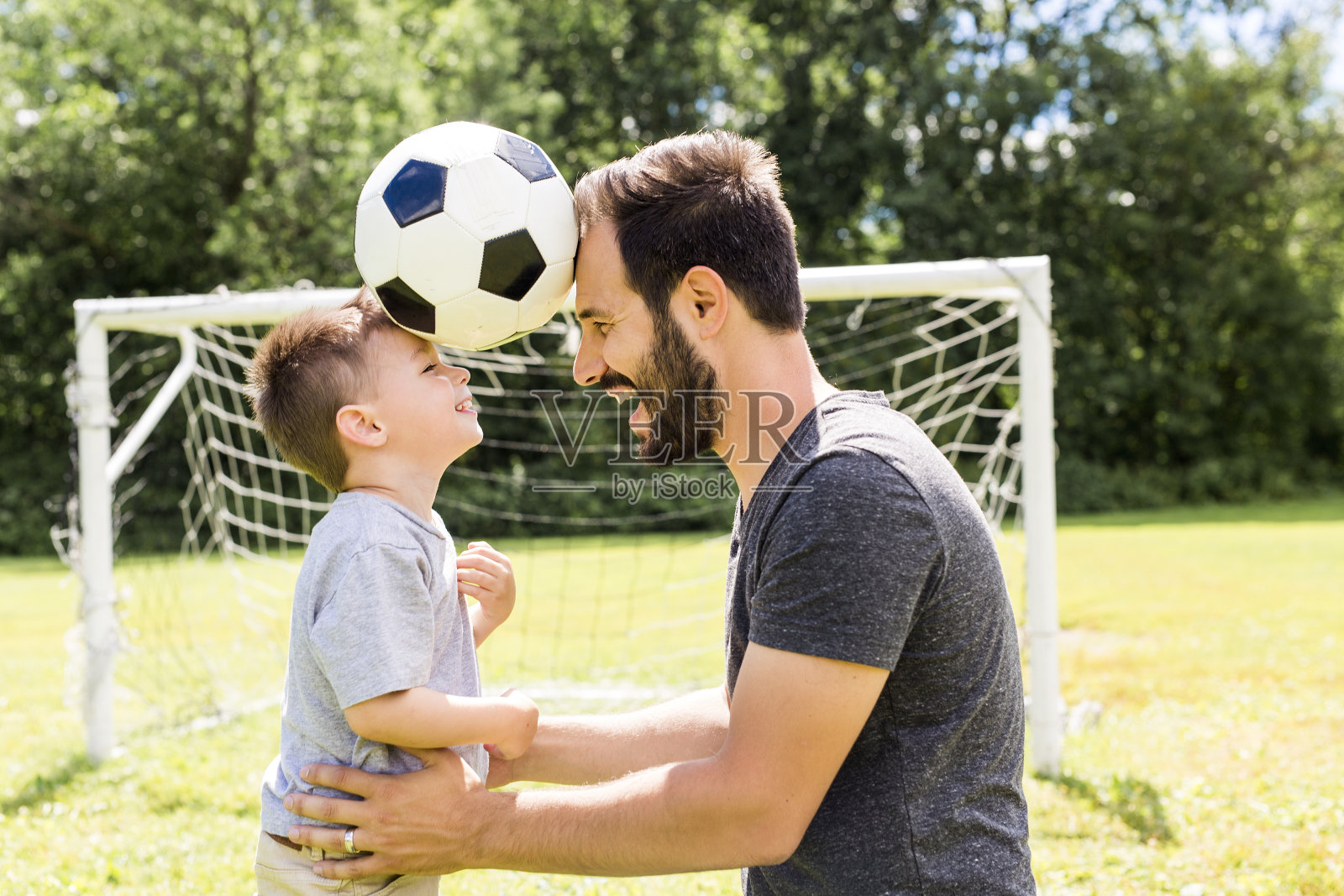 年轻的父亲和他的小儿子在足球场上踢足球照片摄影图片