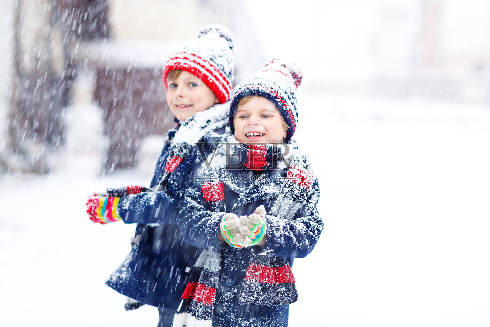 两个小男孩穿着五颜六色的服装在大雪天的户外玩耍。照片摄影图片