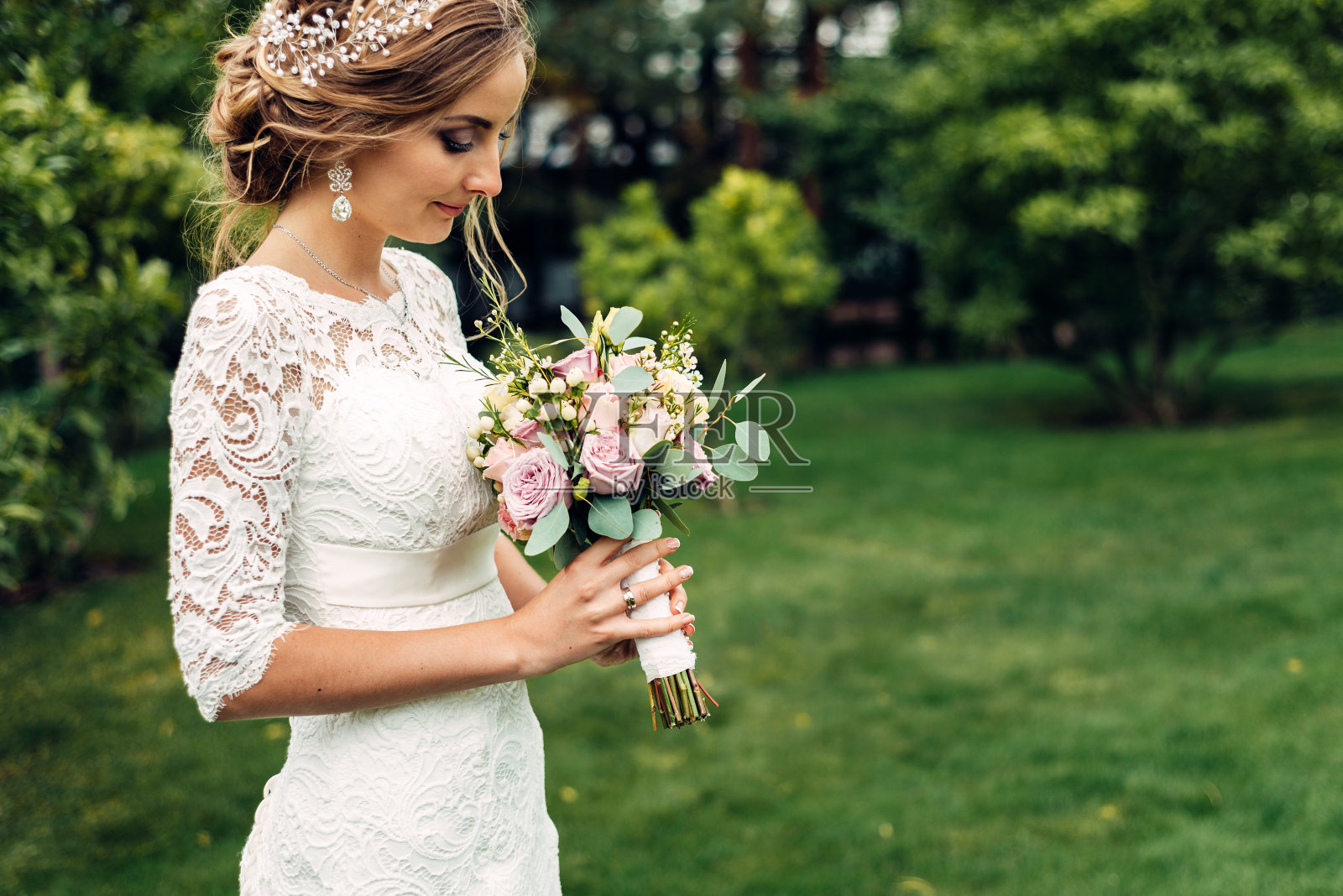 新娘身穿白色长裙，手拿婚礼花束，独自站在那里，看着一束花束等待着她的丈夫照片摄影图片