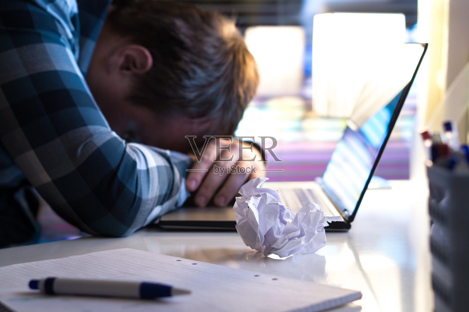 悲伤和疲倦的男人在家里或现代商业办公室晚上。失业的求职者或商人用破纸和笔记本电脑放在桌子上。照片摄影图片
