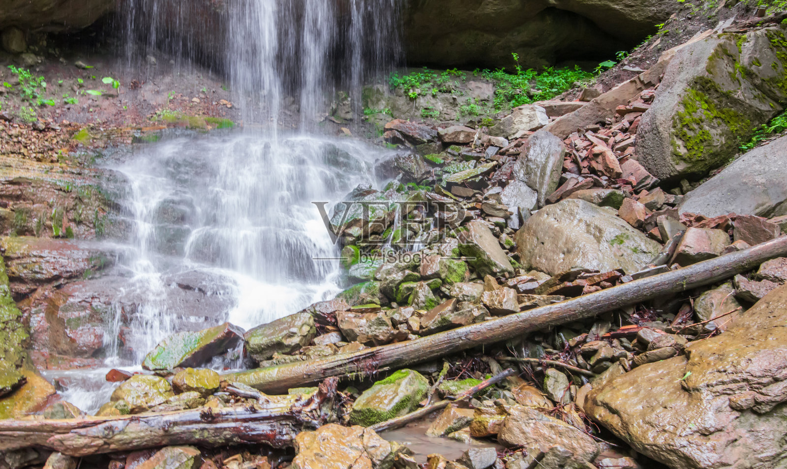 瀑布脚下的巨石和圆木。照片摄影图片
