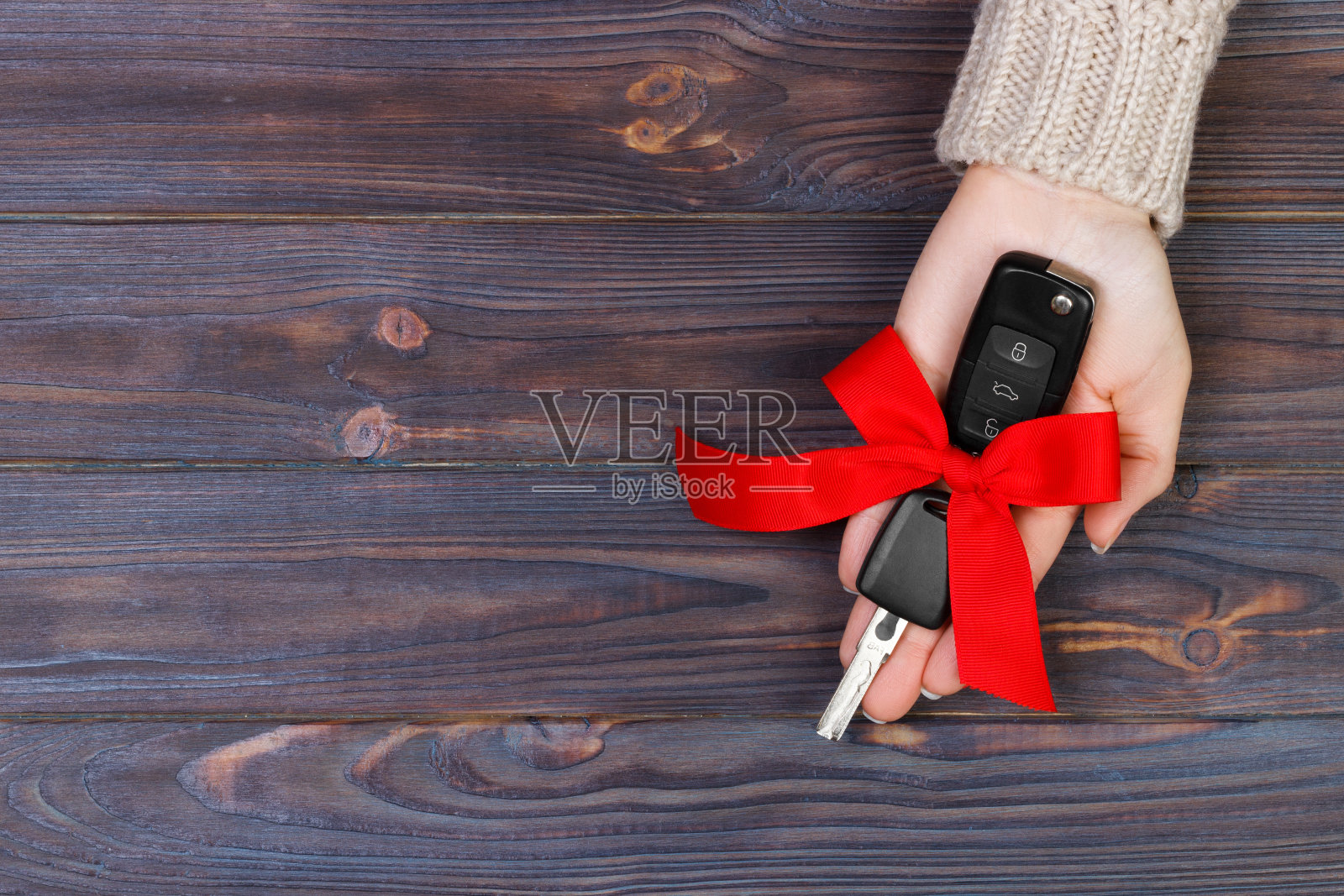女人手里拿着带红色蝴蝶结的车钥匙。送一辆车作为礼物照片摄影图片