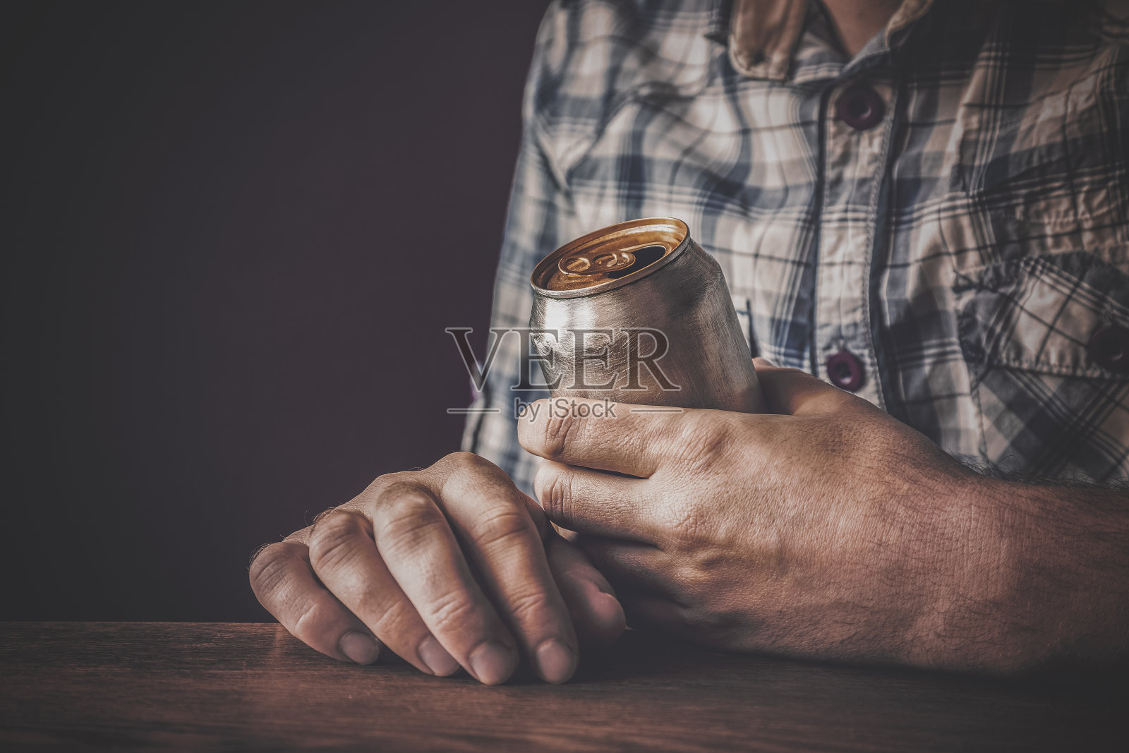 晚上下班后喝冰啤酒的男人。手里拿着一个铝罐。在酒吧或酒吧休息的时间。黑暗压抑的气氛。酒精问题的概念。照片摄影图片