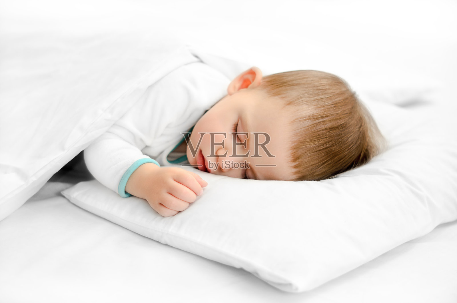 白色背景下熟睡的婴儿。穿着睡衣的小男孩睡在白色的枕头上照片摄影图片