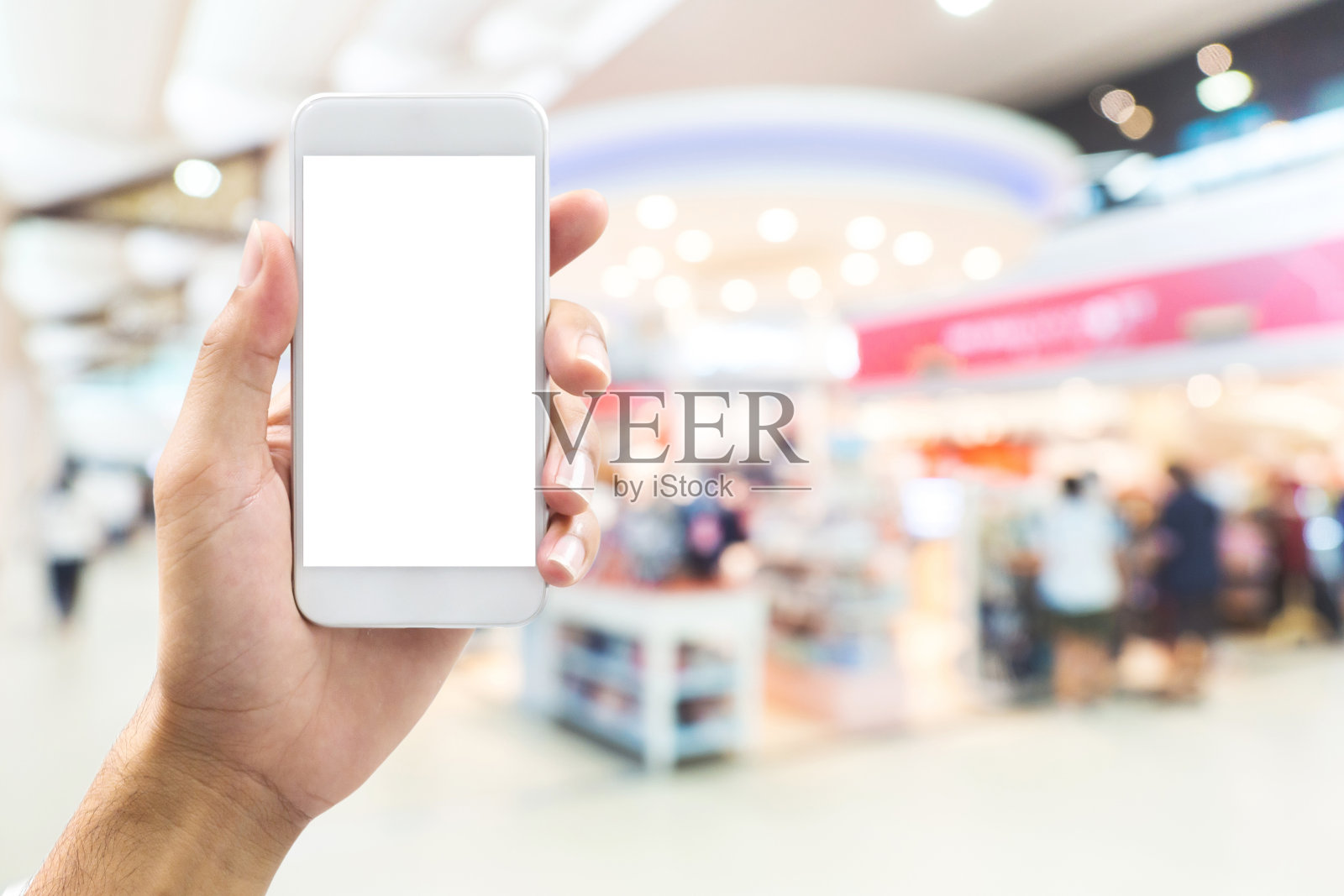 孤立的男子手握智能手机在抽象模糊背景与散景在购物中心，百货公司照片摄影图片