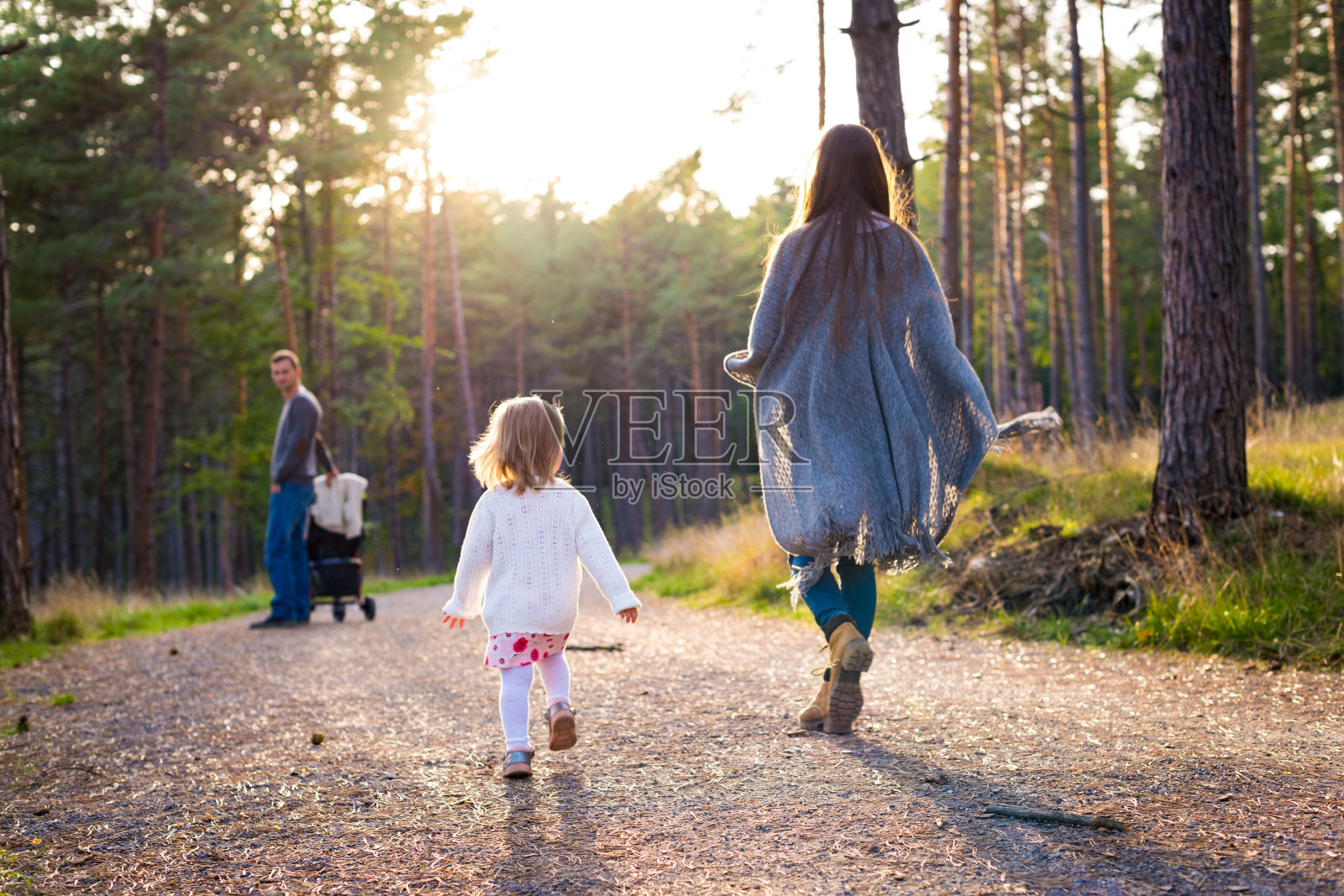 快乐的年轻家庭在公园散步，后视镜。一家人和他们的女儿一起走在福勒斯特小路上，父亲推着婴儿车。照片摄影图片